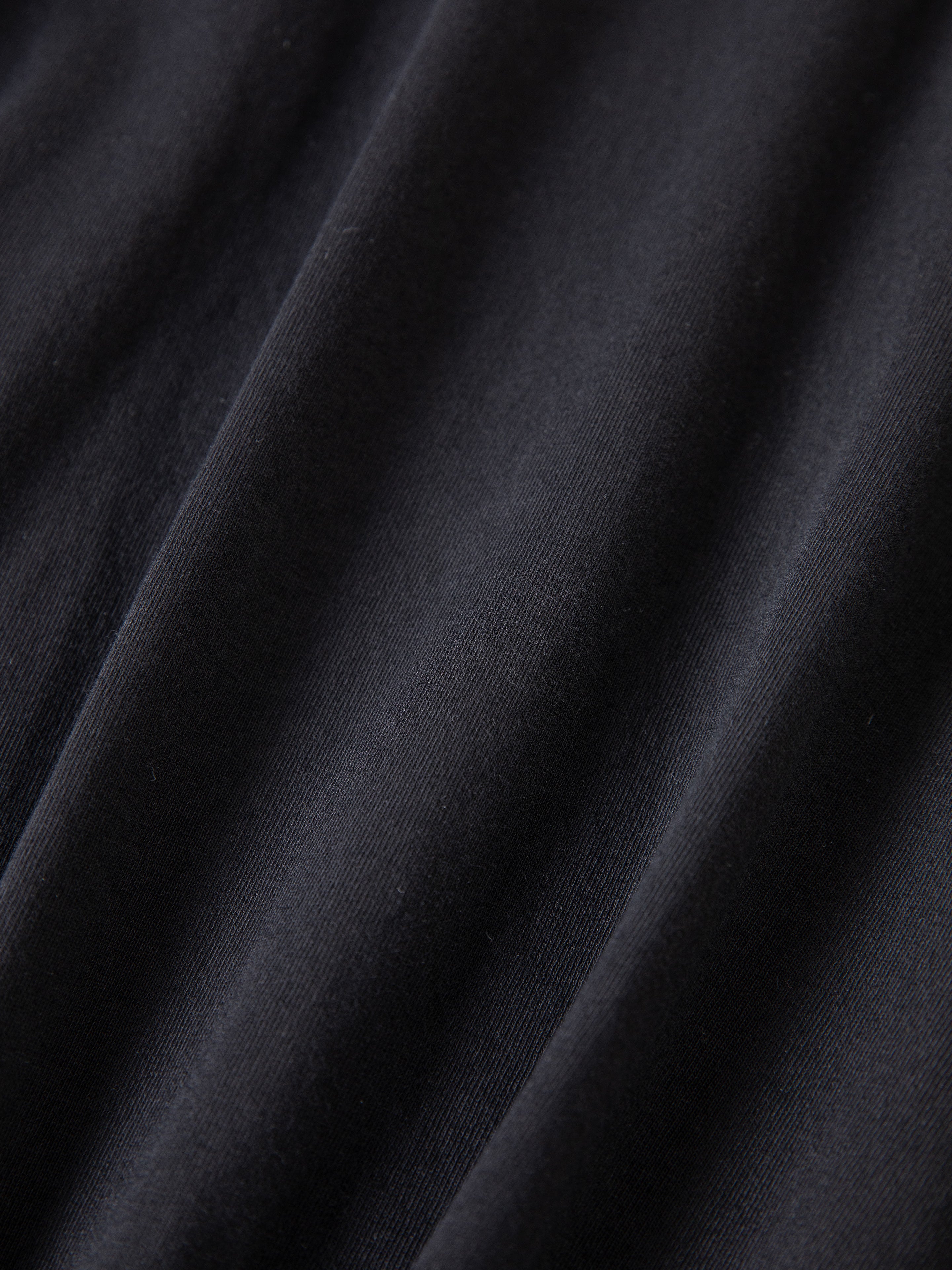 Close-up of smooth black fabric from the FOUND Reversed LS Tee, showing soft folds and subtle diagonal lines for a relaxed, unisex fit.