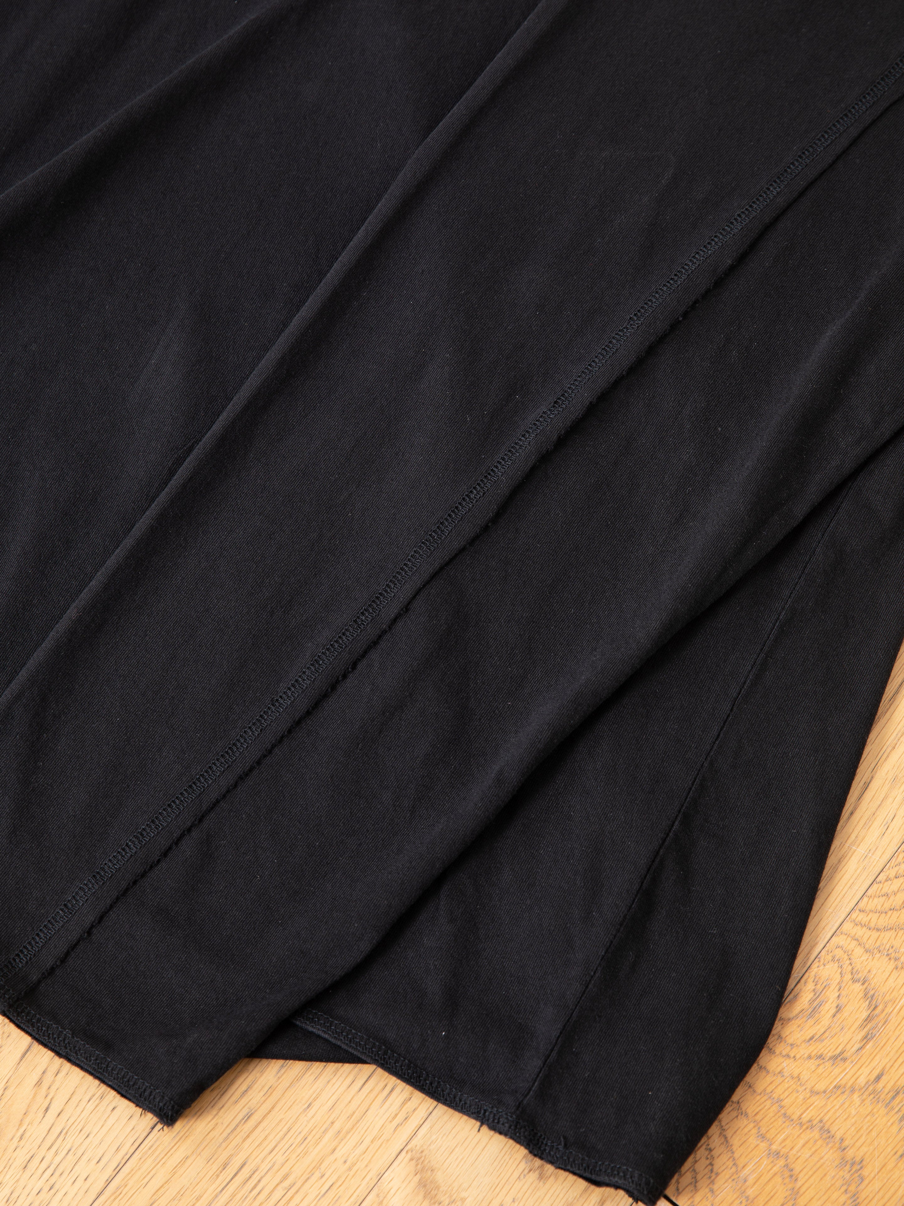 A close-up of black fabric with visible seams, likely from a FOUND Reversed LS Tee, laid out on a wooden floor—an essential unisex staple for any casual wardrobe.