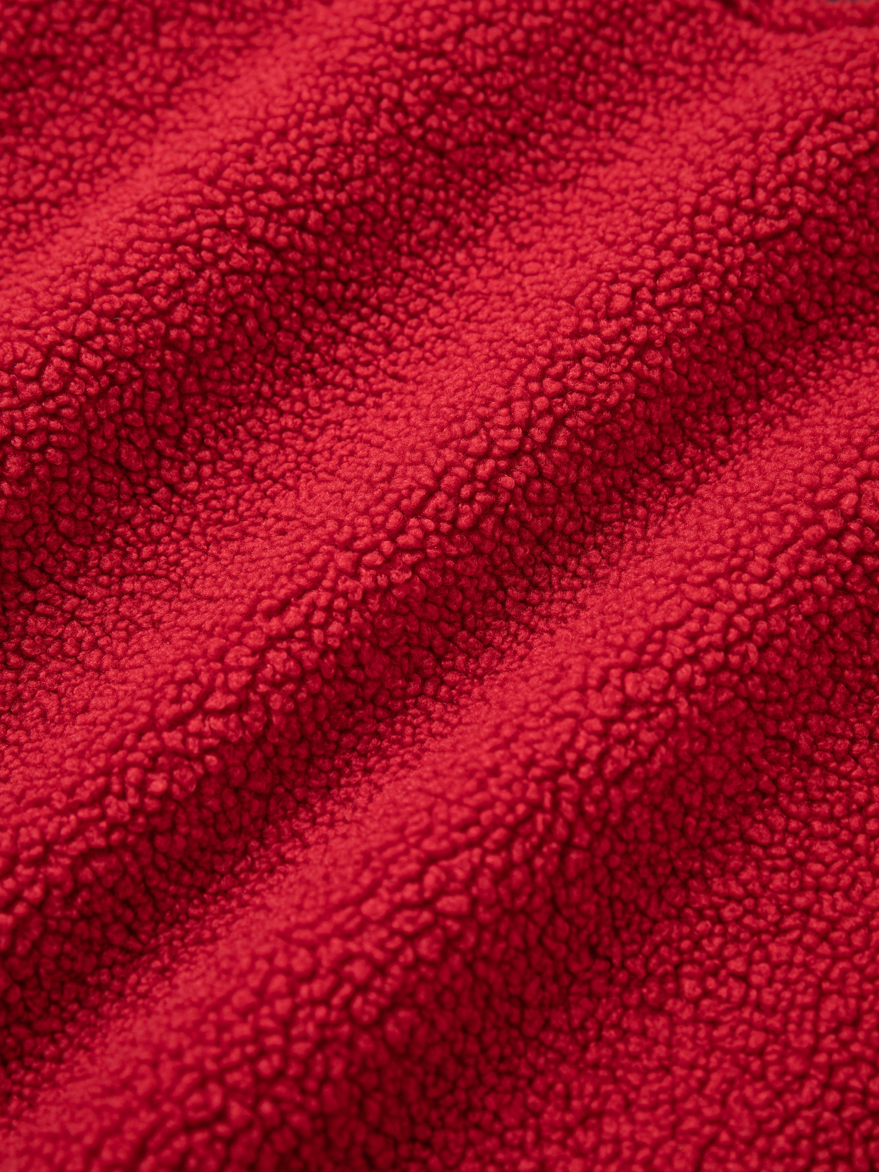 Close-up of the Pahari Floral Embroidered Sherpa Pullover by FOUND, featuring red textured fabric with a sherpa-like appearance. The fabric showcases small, soft, rounded bumps and gentle folds, reminiscent of the fine detail found in Pahari style embroidery.