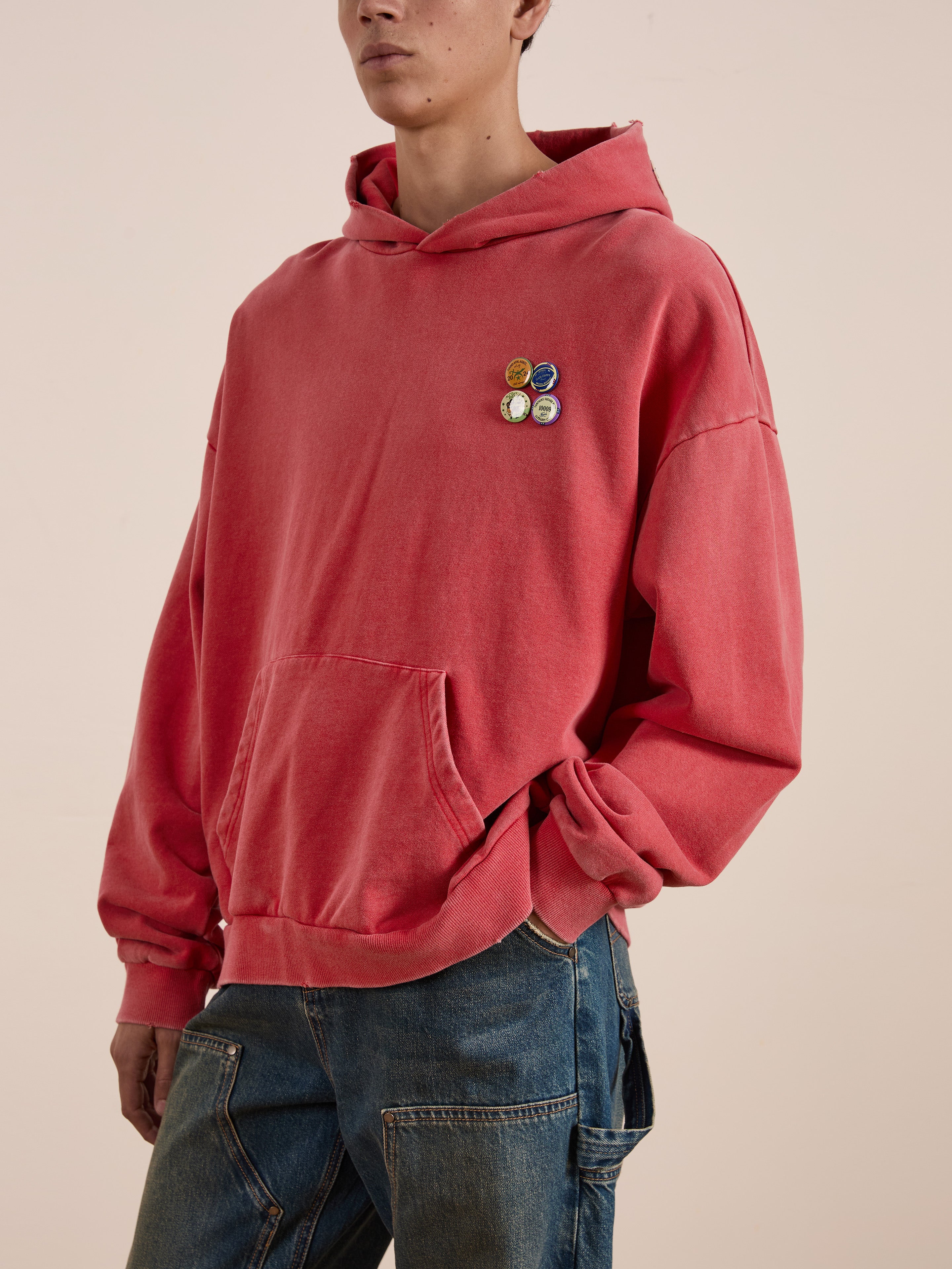 A person in a FOUND Multi Patch Hoodie with four decorative pins on the chest is wearing sun-faded wash blue jeans.
