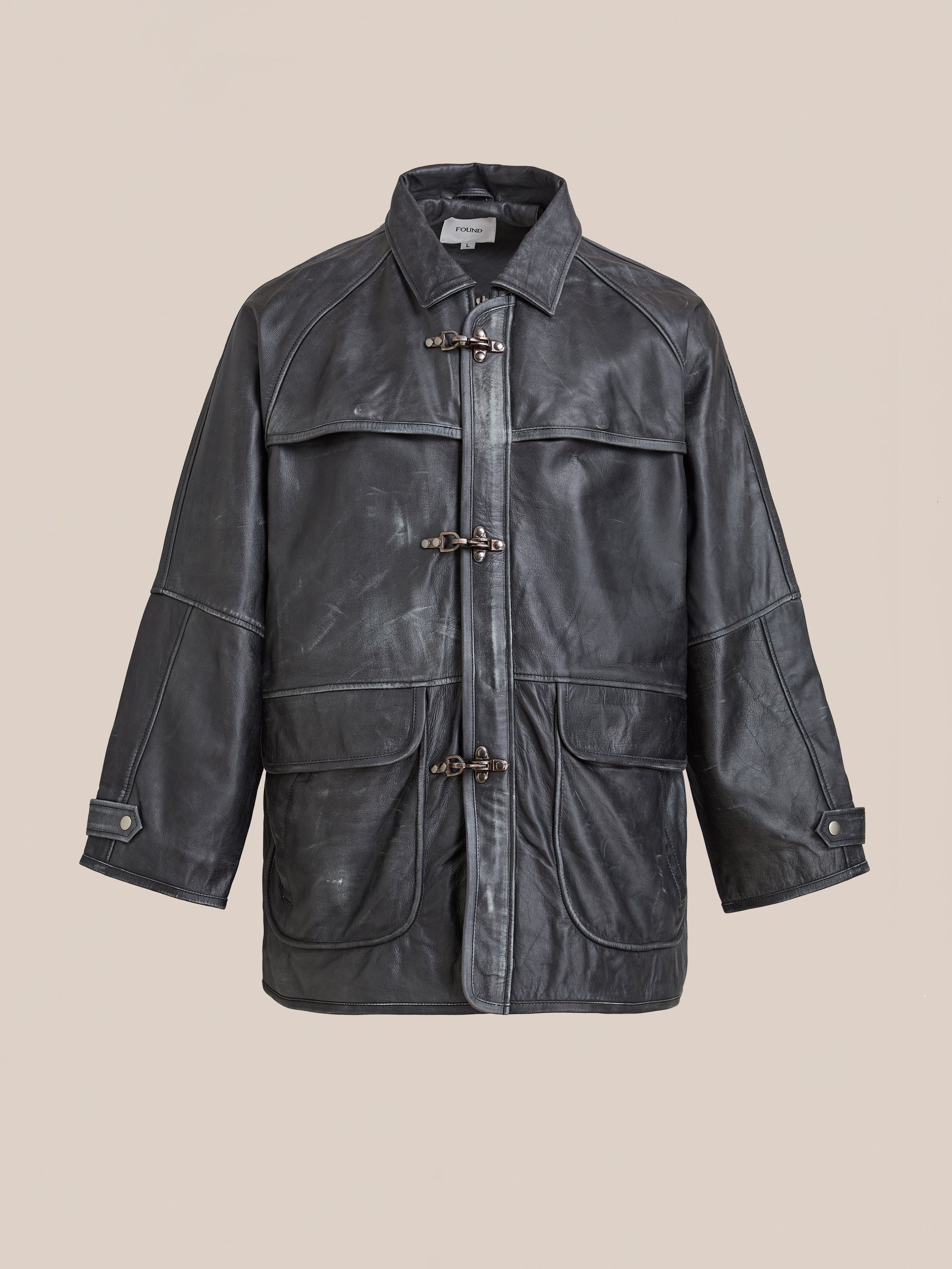The FOUND Distressed Leather Fireman Clasp Jacket features toggle closures, large front pockets, and wide sleeves. Displayed against a plain beige background, this unisex jacket blends style with practicality.