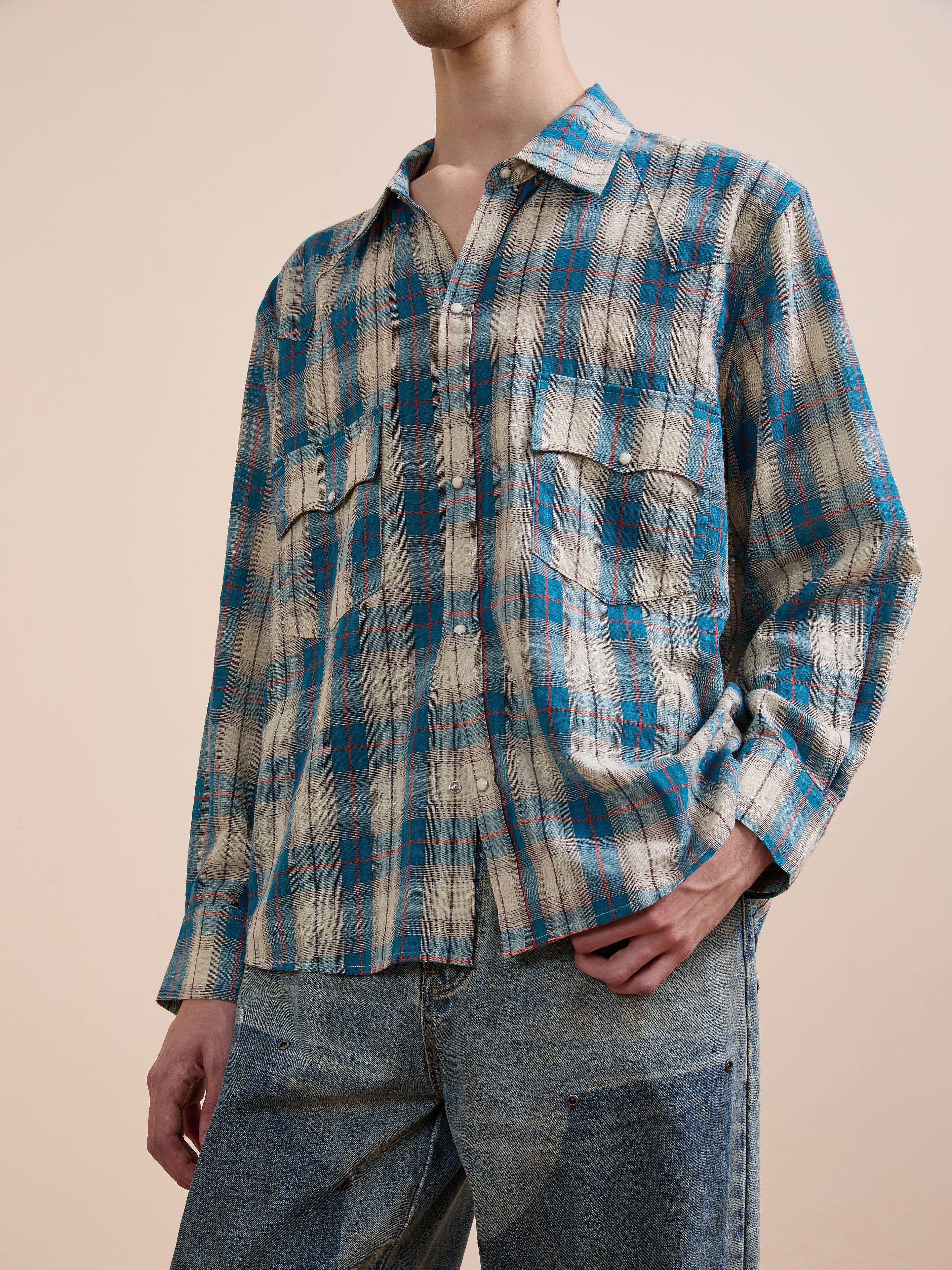 A person wears the FOUND Flannel Shirt in blue and beige plaid with chest pockets and light blue jeans, standing against a plain background. This unisex relaxed fit offers timeless classic Americana style.