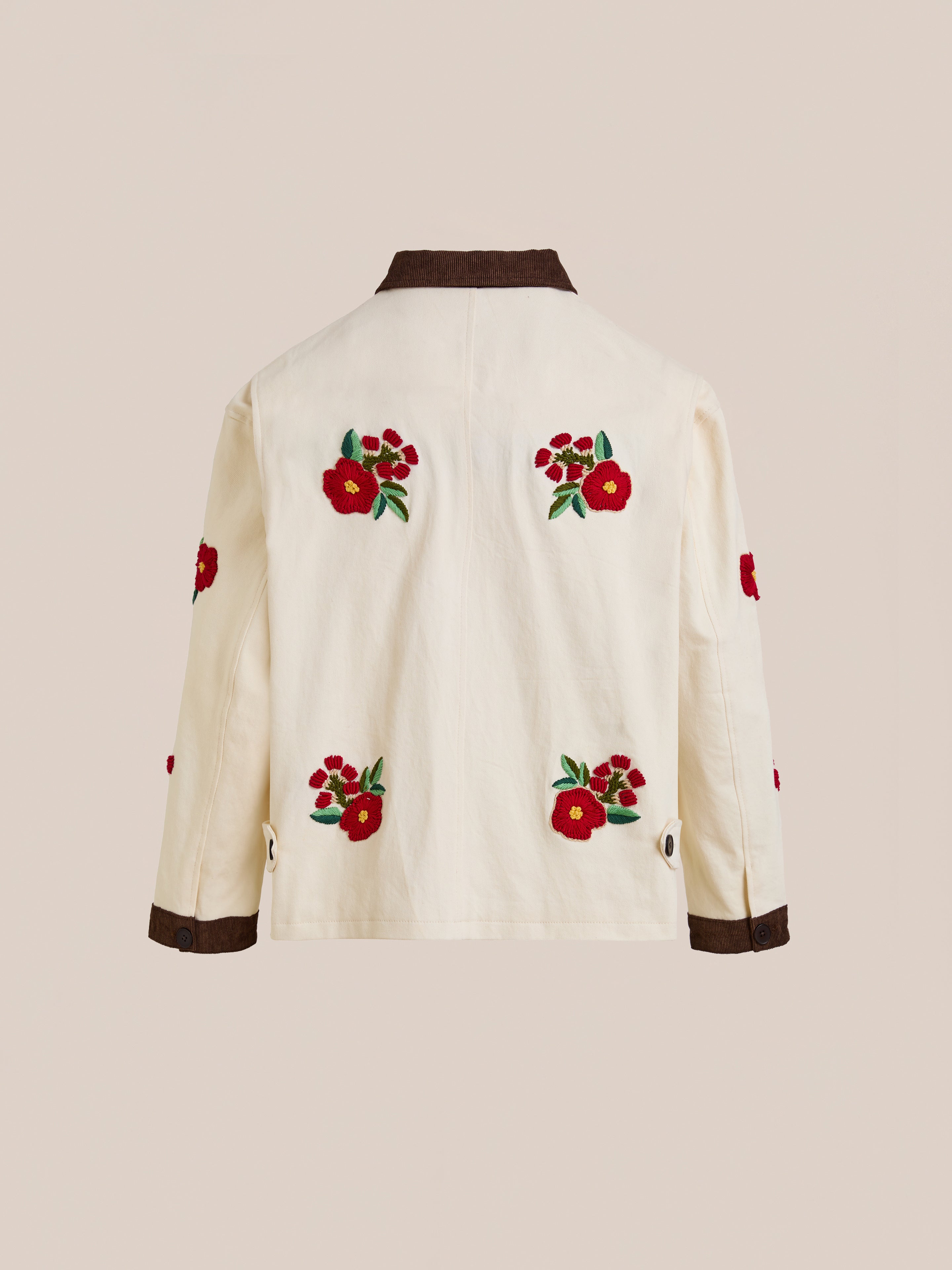 The Found Floral Hand Embroidered Work Jacket features cream fabric with red and green floral embroidery on the back and sleeves, vintage South Asian-inspired details, and brown cuffs and collar.