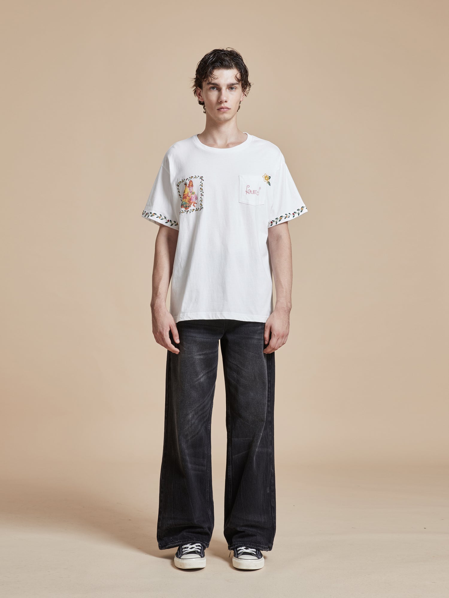 A man wearing a Found Flower Children Tee and black pants.