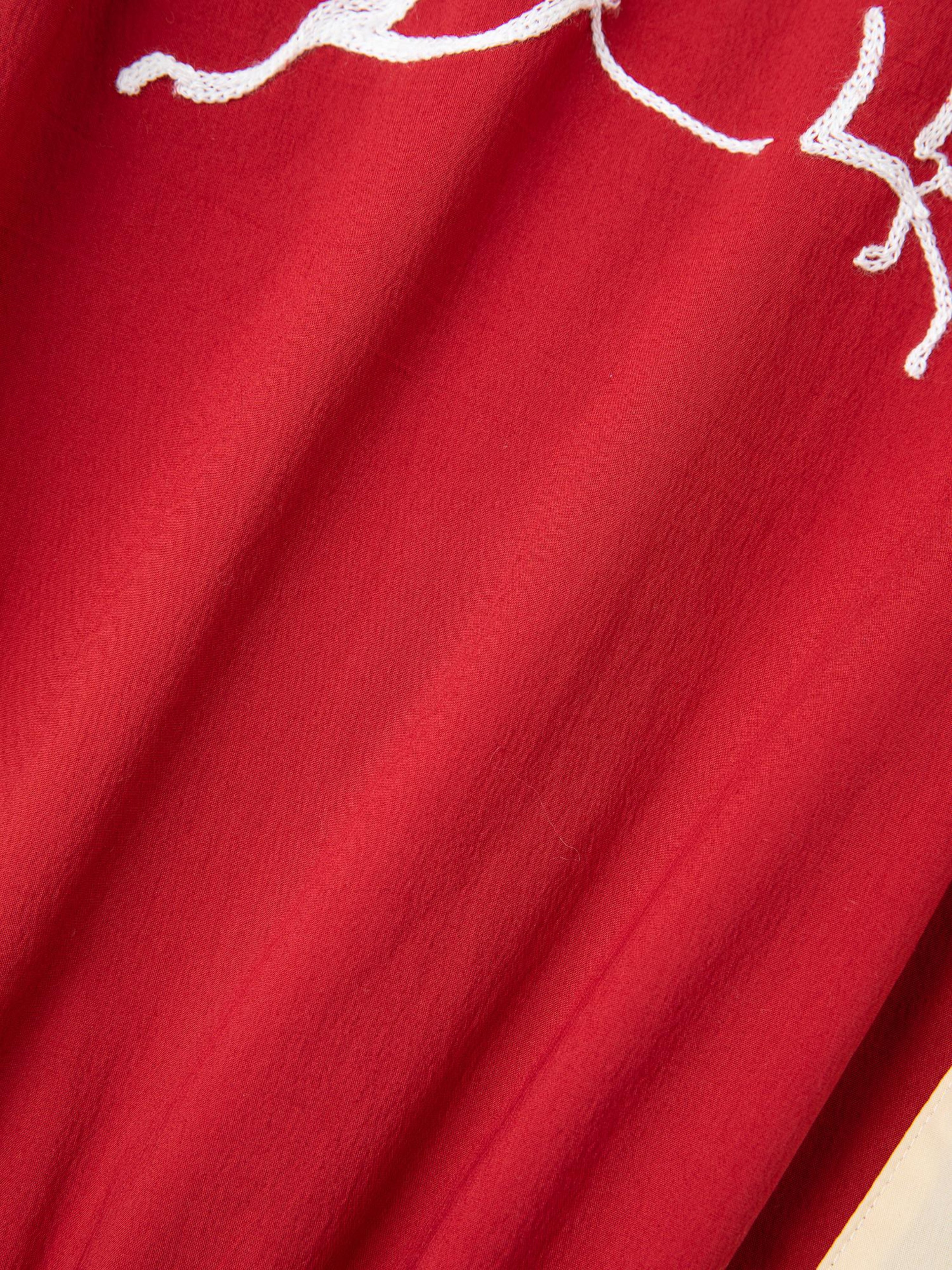 Close-up of red fabric with a white embroidered pattern, reminiscent of the intricate designs on the FOUND Pine and Rose Track Jacket, blending elegance with sportswear flair.