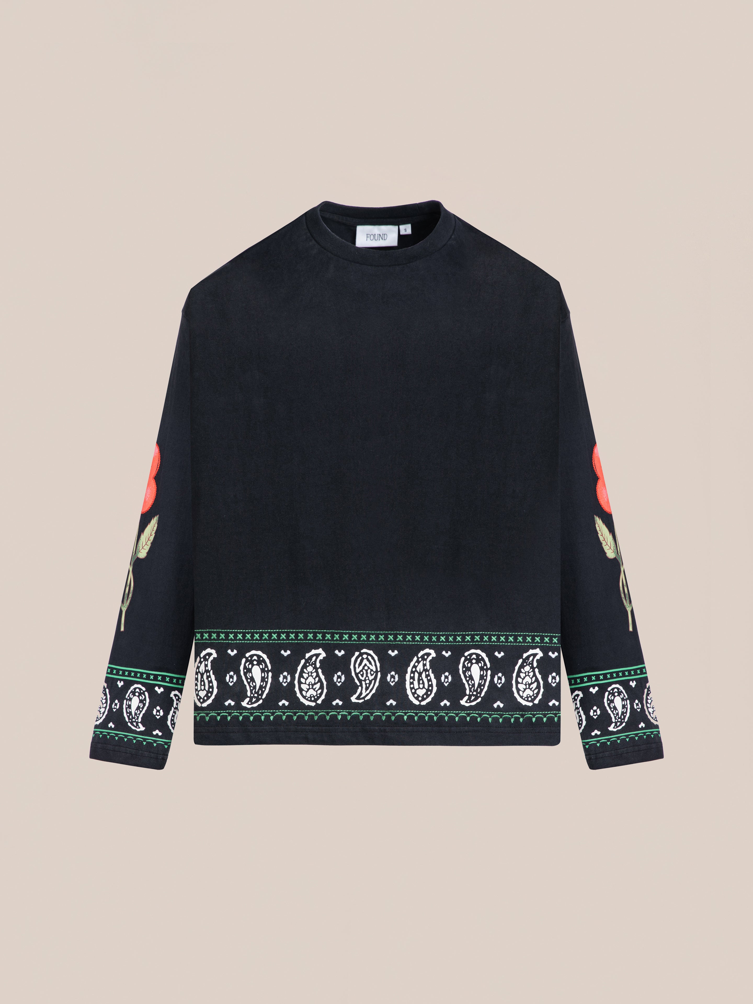 The FOUND Garden Bloom Embroidered LS Tee features a relaxed fit, black long sleeves with red rose embroidery, and white paisley plus green border details on the hem and cuffs, shown against a plain background.