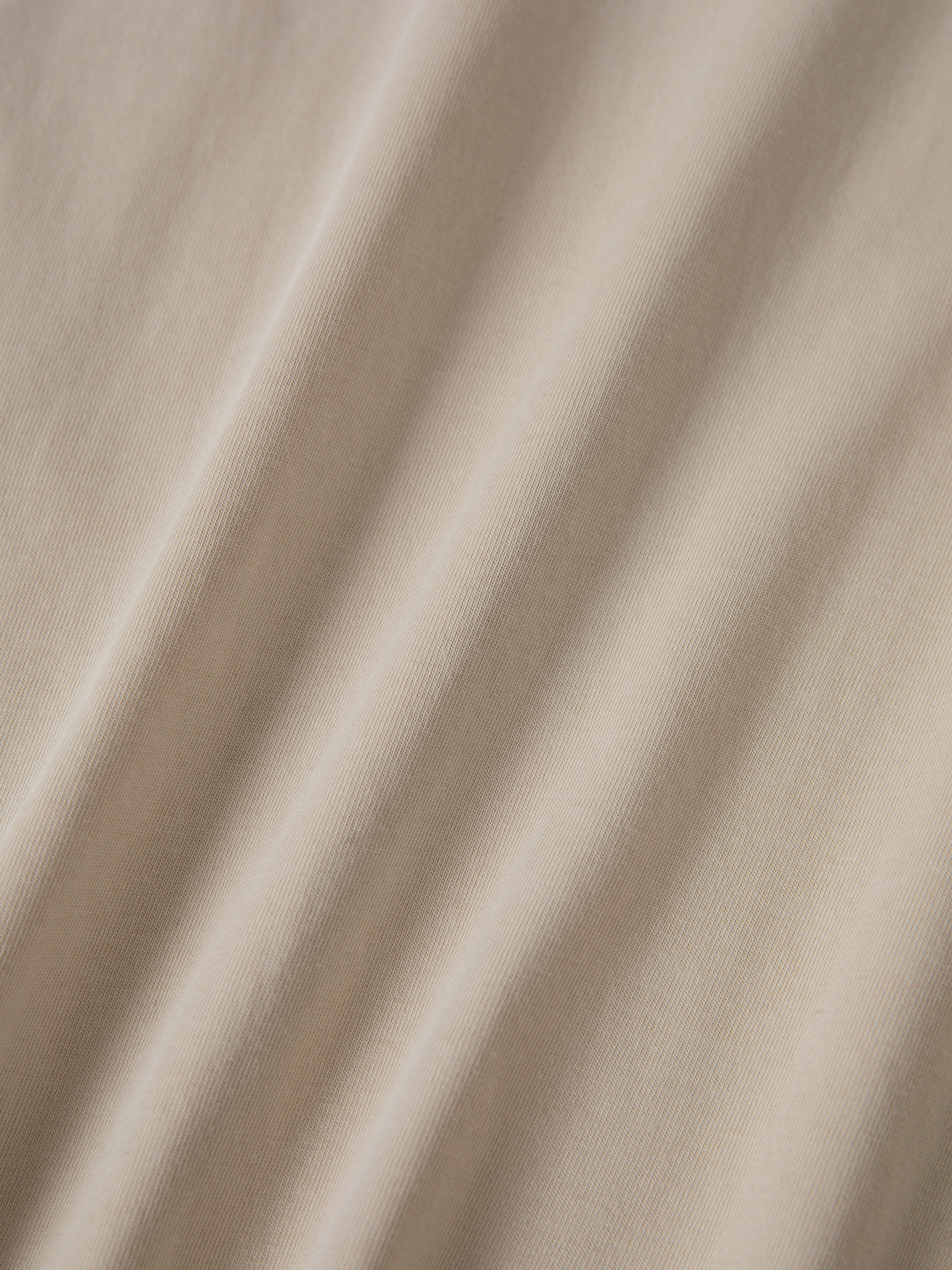 Close-up of light beige fabric with soft diagonal folds, subtle texture, and delicate embroidered floral graphics, featured on the unisex FOUND Garden Bloom Embroidered LS Tee.