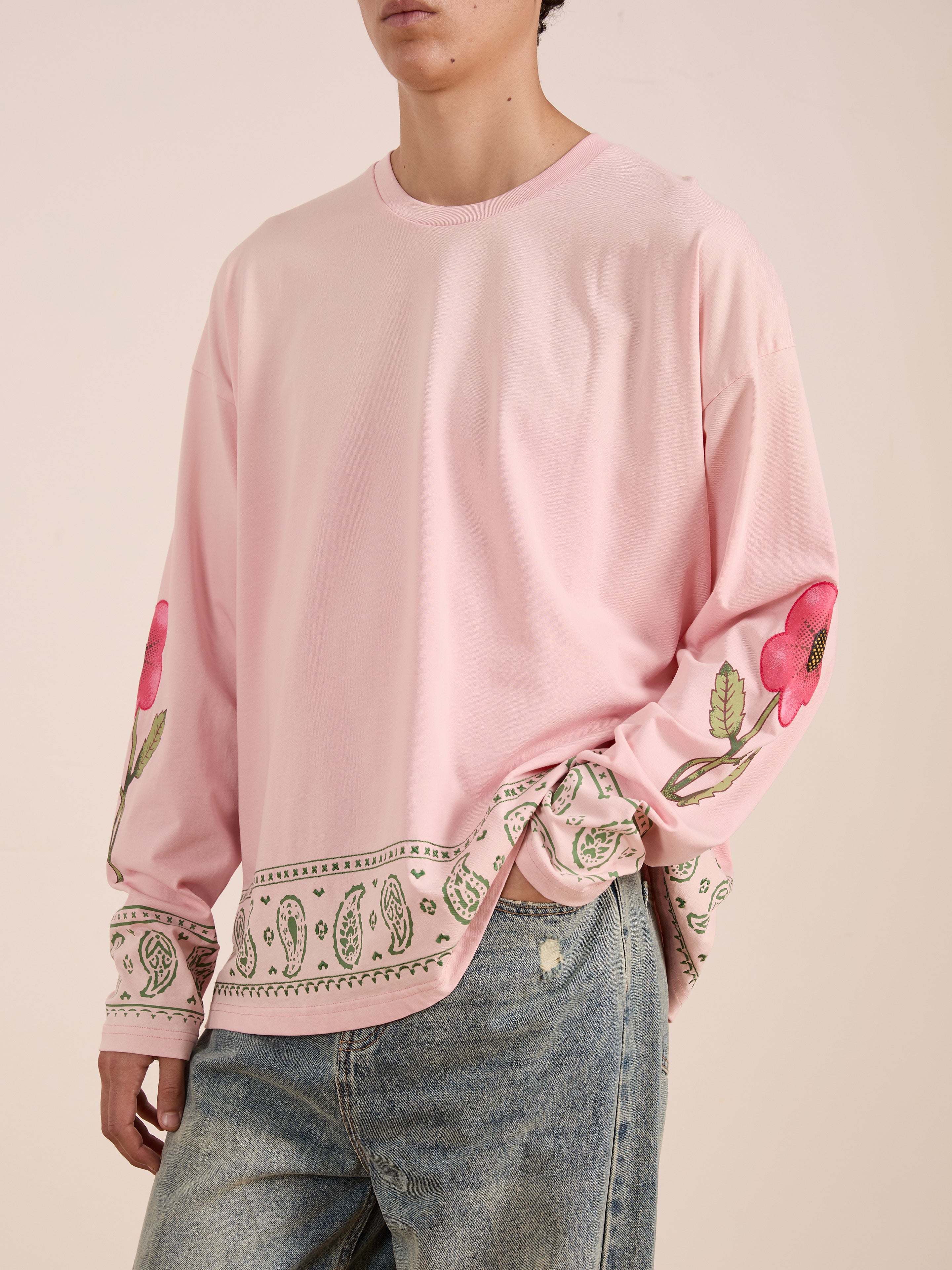 A person wears the FOUND Garden Bloom Embroidered LS Tee, featuring floral and paisley embroidery, paired with light blue jeans against a plain background. This unisex relaxed-fit top delivers effortless style.