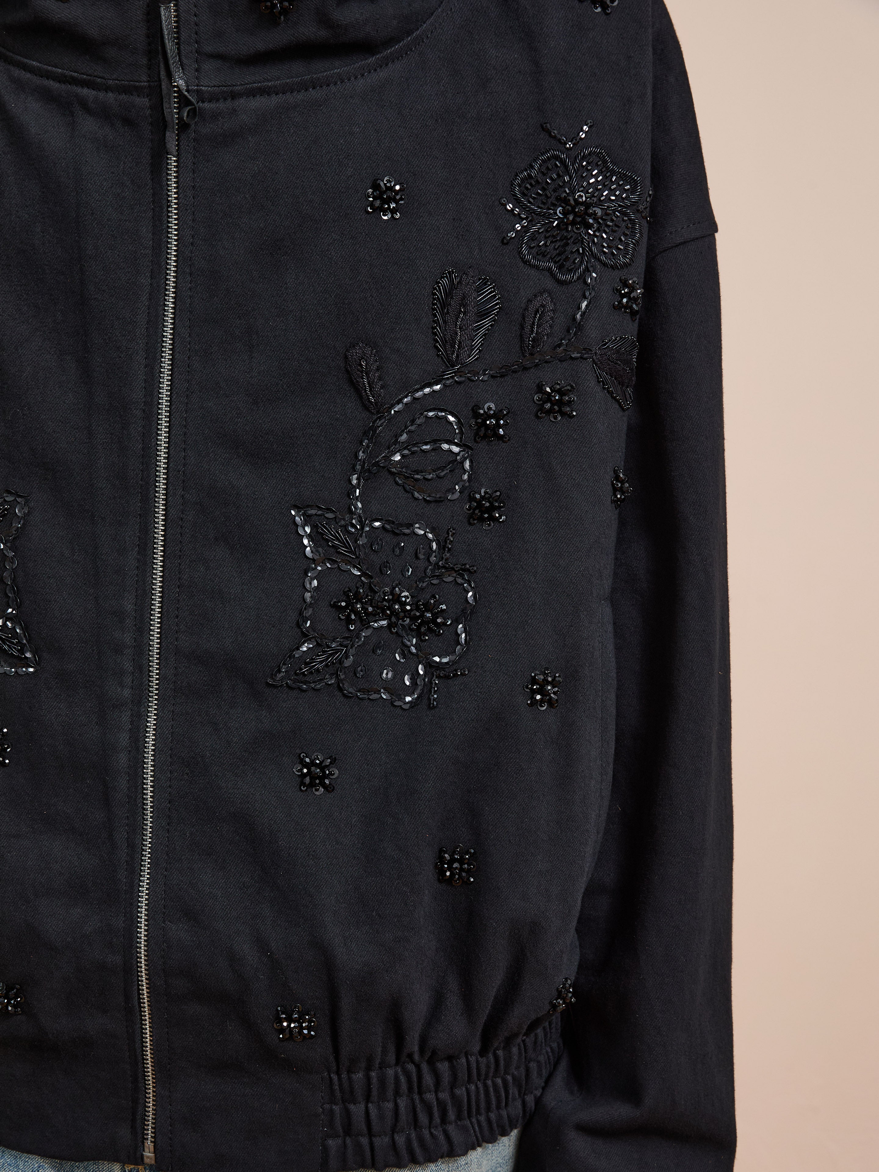 A close-up of the FOUND Hand Embroidered Tonal Anorak Jacket showcases intricate black bead and sequin floral embroidery, with delicate beaded accents on the front highlighting its exquisite craftsmanship.