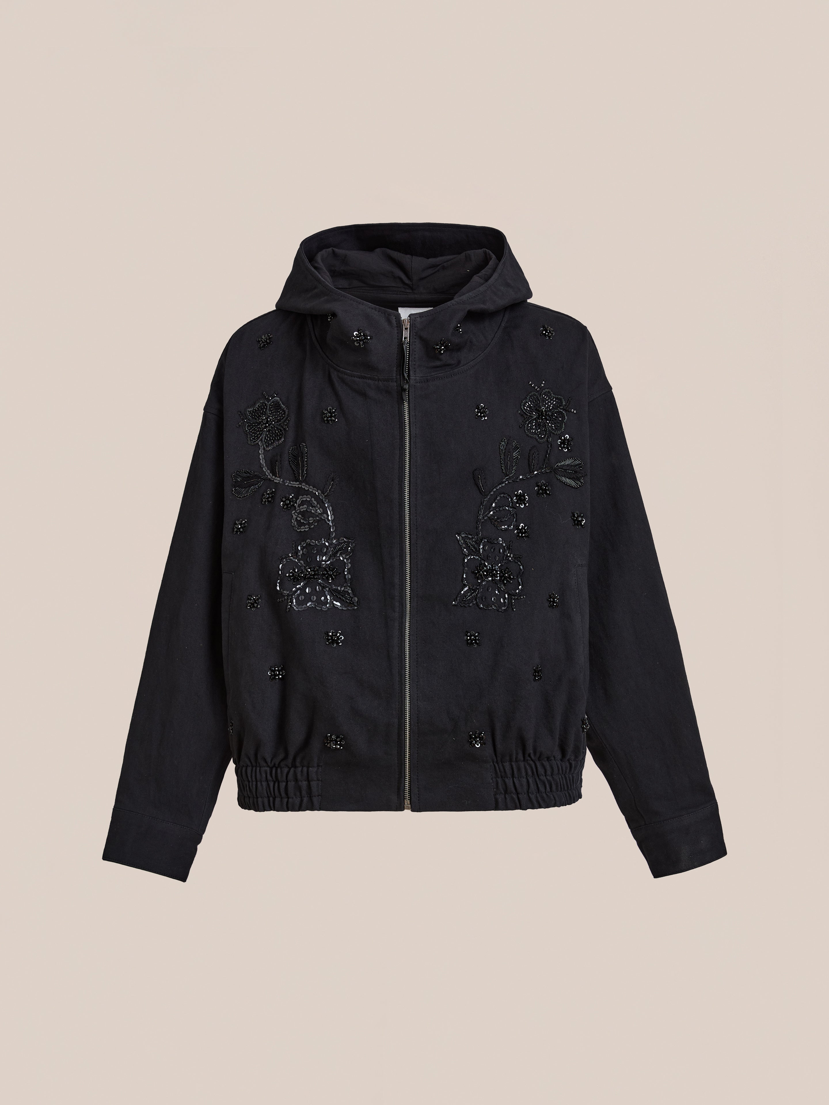 The FOUND Hand Embroidered Tonal Anorak Jacket is a black hooded zip-up with an elastic hem, detailed with floral beadwork and intricate front embroidery—blending artisanal charm with modern style.
