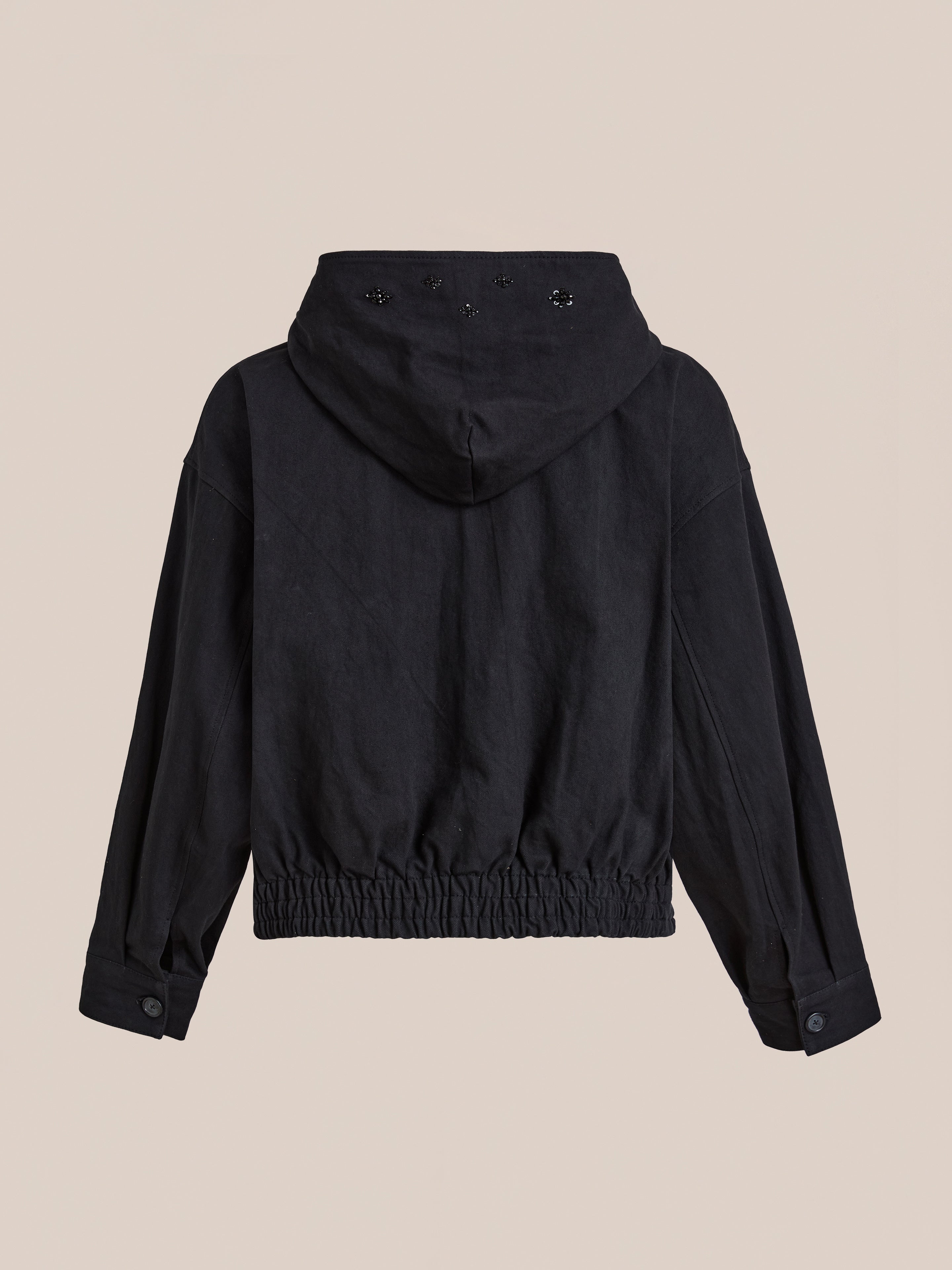 A black FOUND Hand Embroidered Tonal Anorak Jacket shown from the back features a gathered elastic waistband, buttoned cuffs, hood eyelet details, and subtle floral beadwork for an elegant touch.