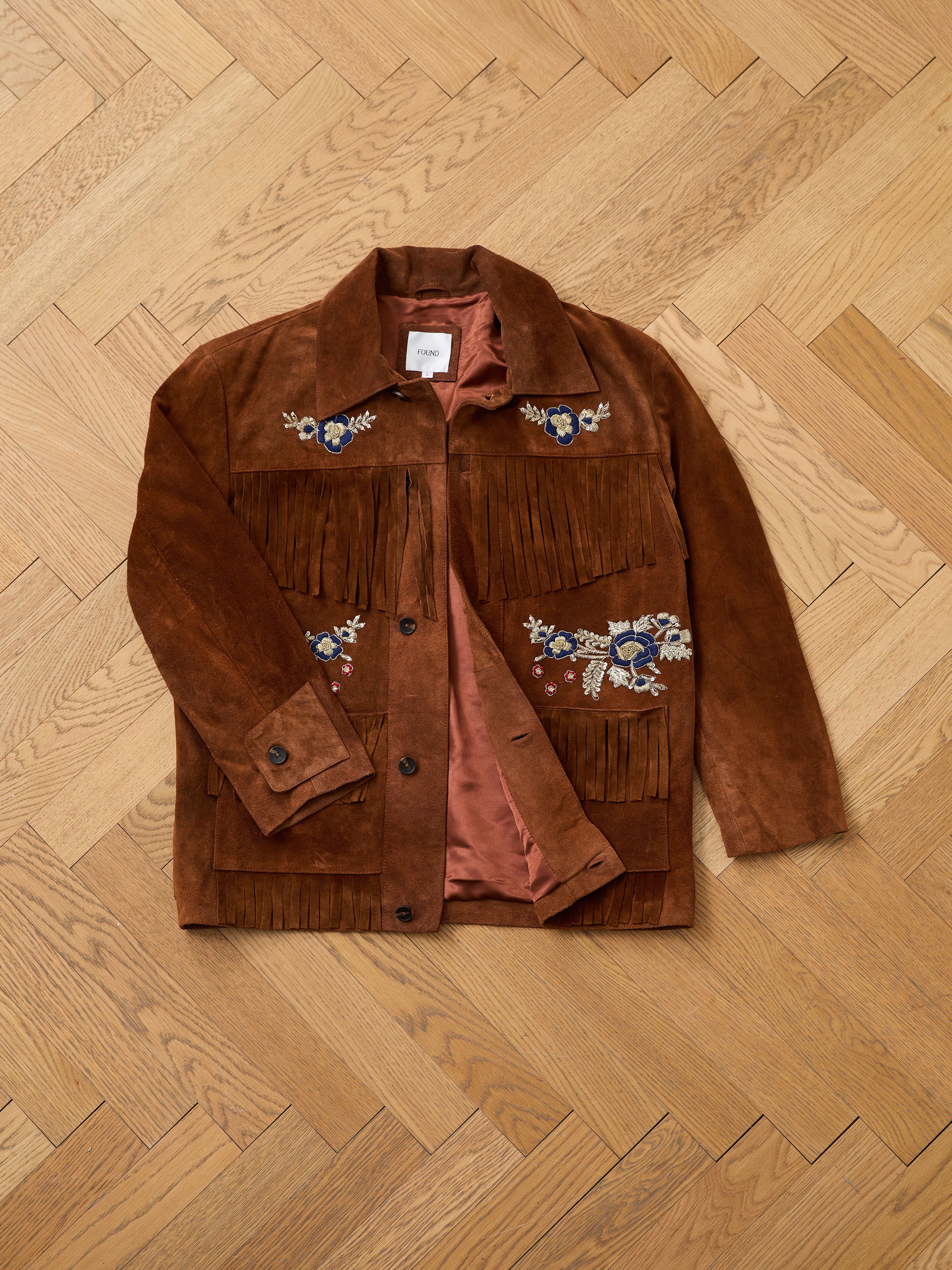 FOUND Hand Embroidered Suede Fringe Jacket in brown, featuring floral embroidery, displayed flat on a light wooden parquet floor.