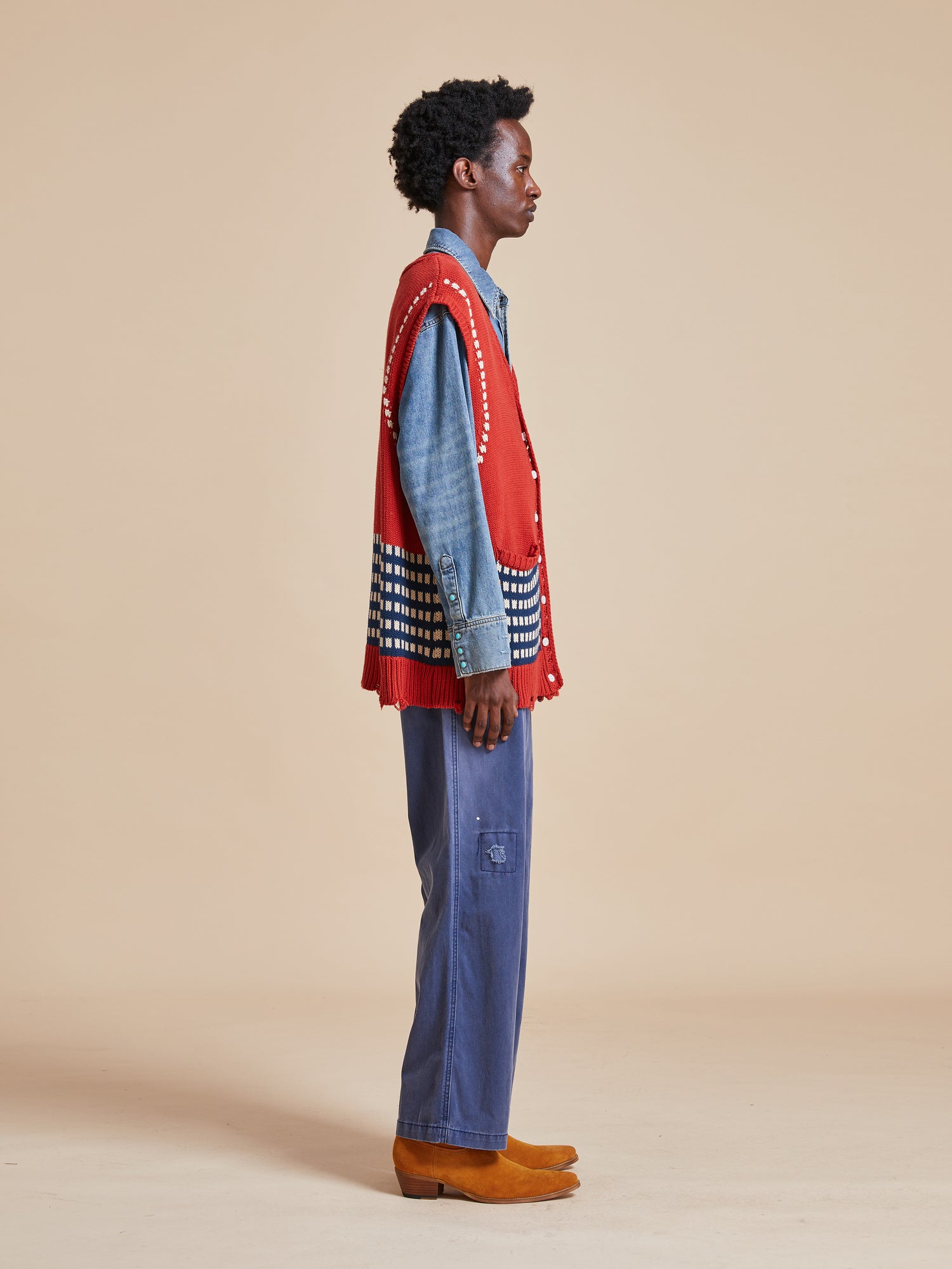 A man wearing a Homestead Check Sweater Knit Vest by Found and blue pants.