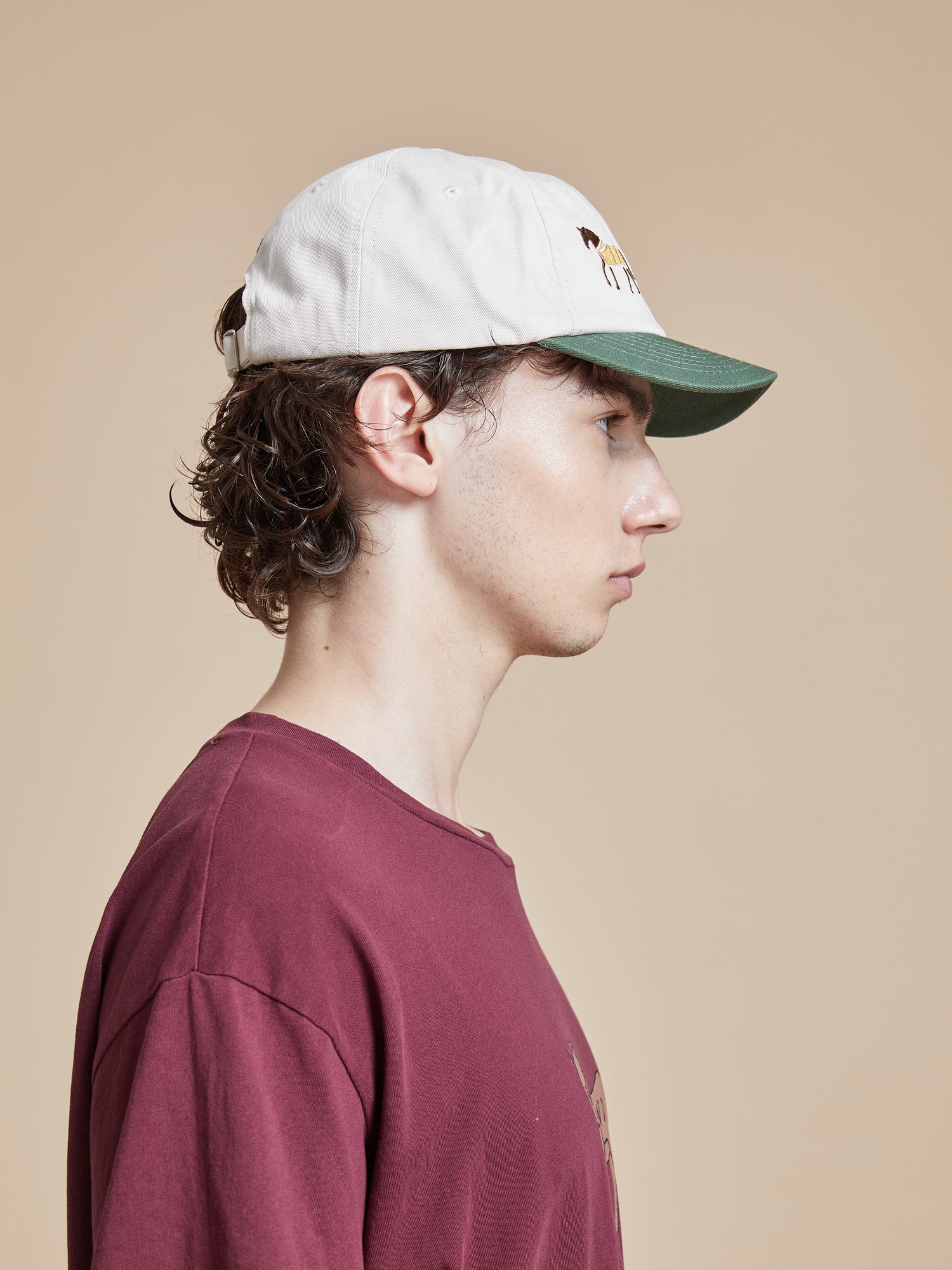 A man wearing a burgundy t-shirt and a white Found Horse Equine Cap.