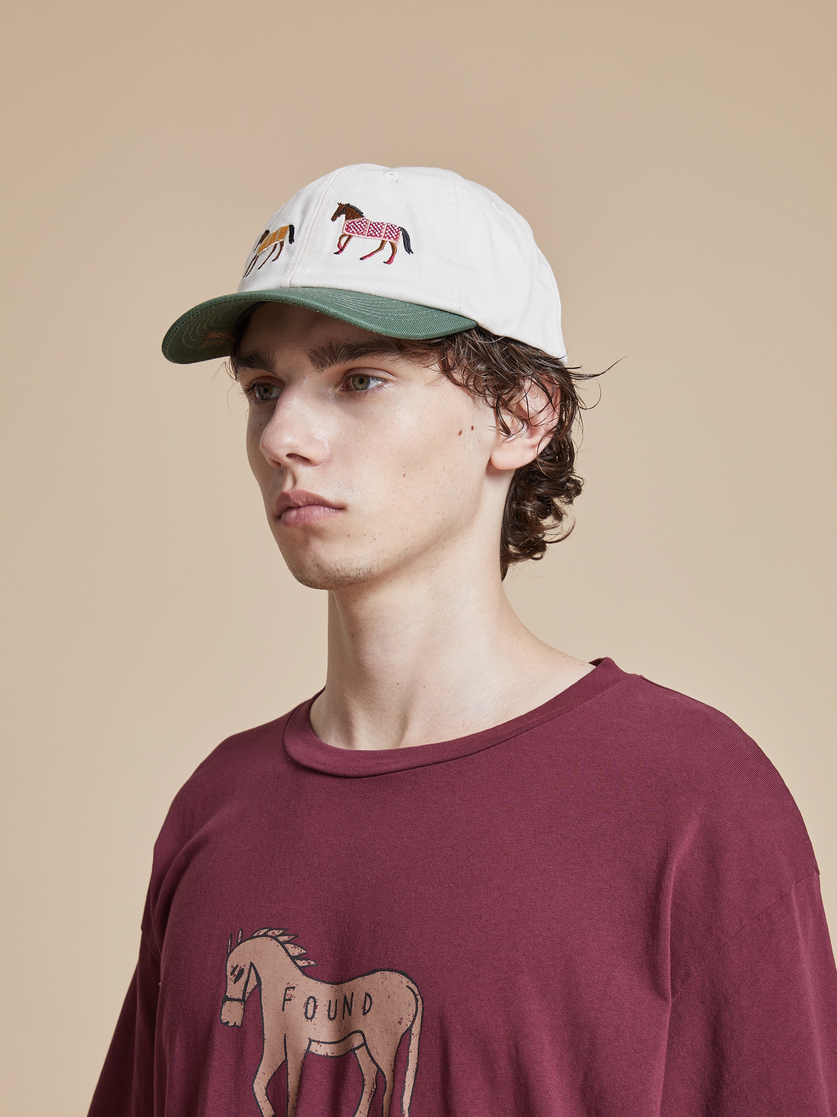 A young man wearing a burgundy t - shirt with a Found Horse Equine Cap on it.