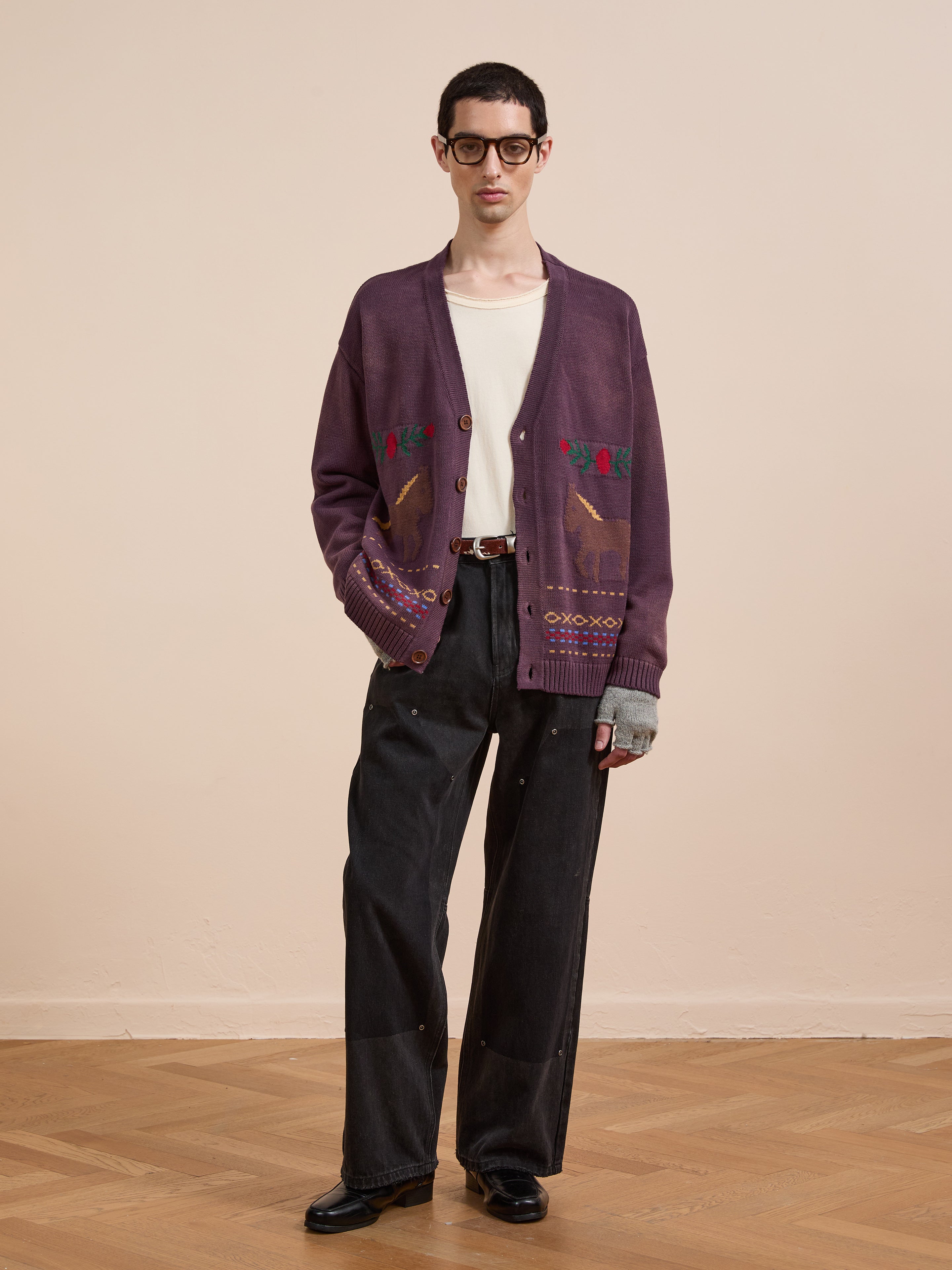 Indoors, a person wears glasses, a white shirt, Found's Horse Jacquard Cardigan with animal motifs, black wide-leg pants, and black shoes.