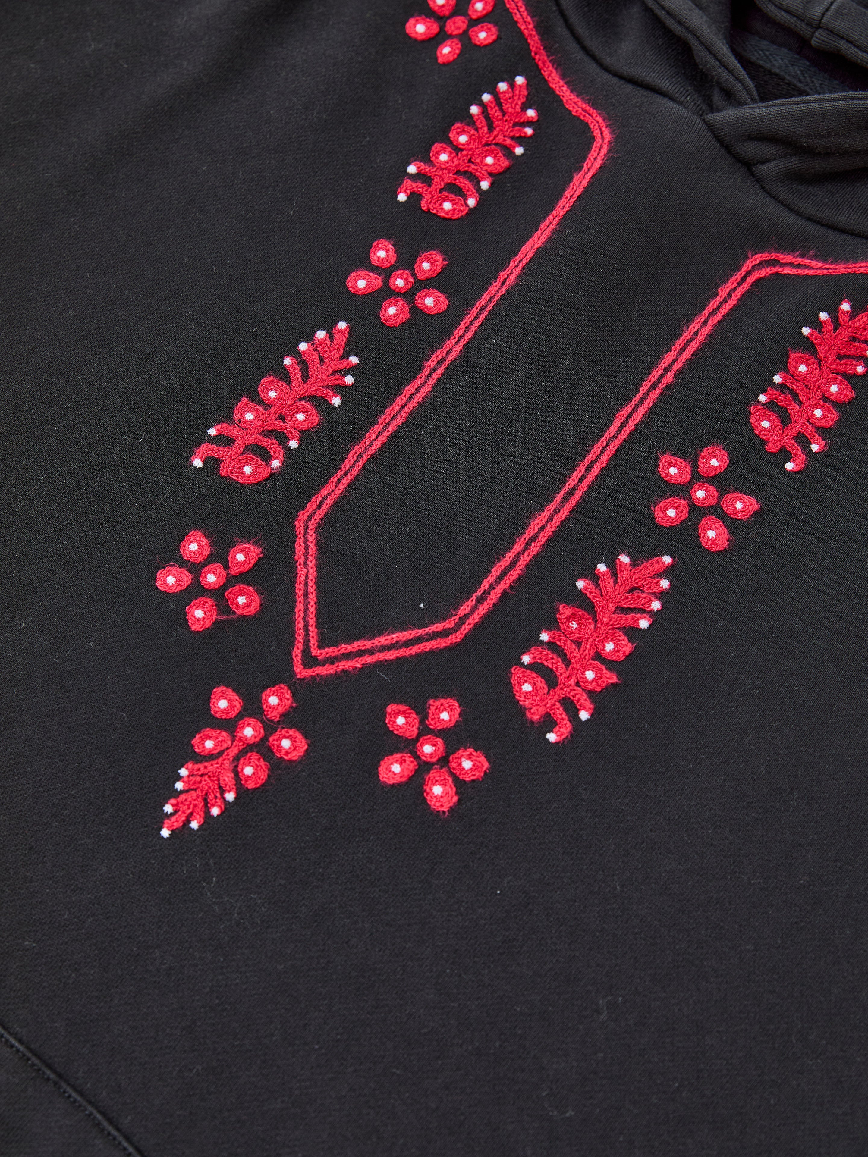 Close-up of the FOUND Indus Embroidered Hoodie: black fabric adorned with red floral embroidery and detailed white geometric patterns in a symmetrical, vintage-inspired design.