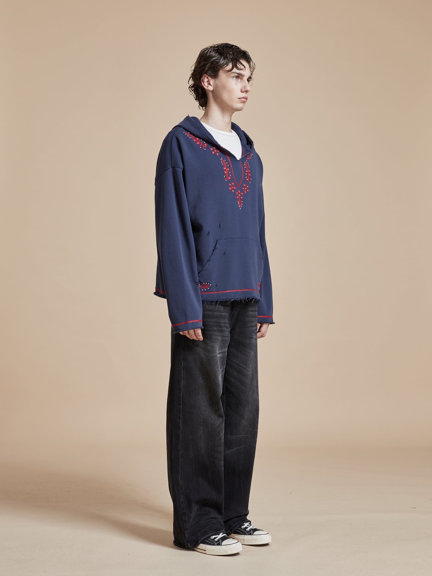 A man wearing an Indus Embroidered Hoodie by Found and black pants.