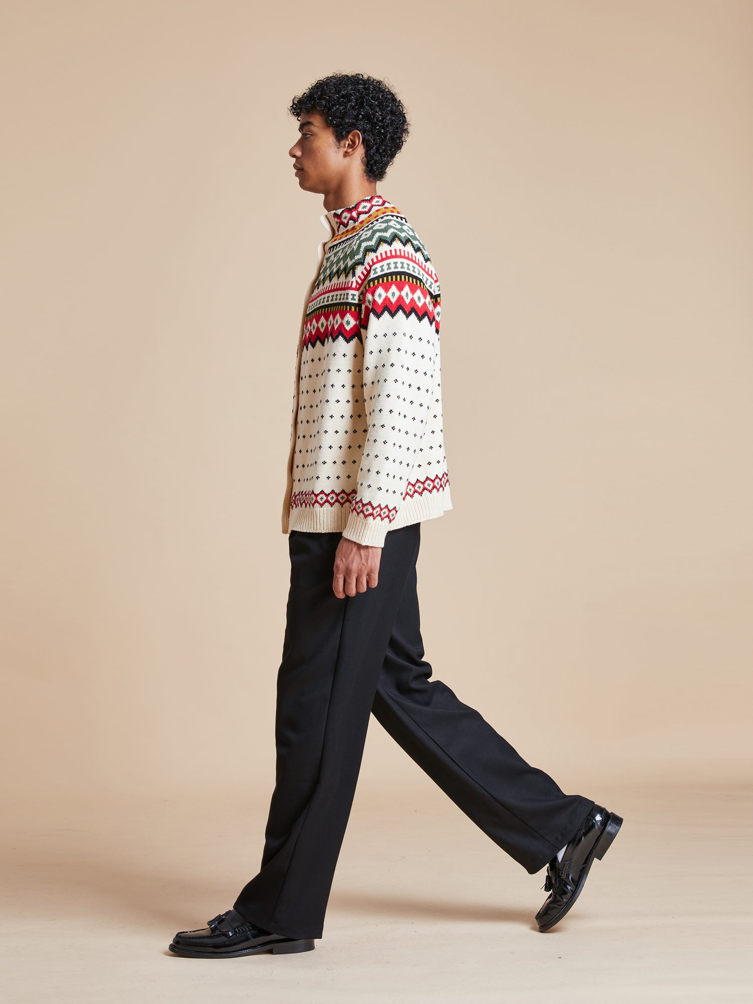 A man in a Harwan Isles Sweater from the Found brand walking on a beige background.