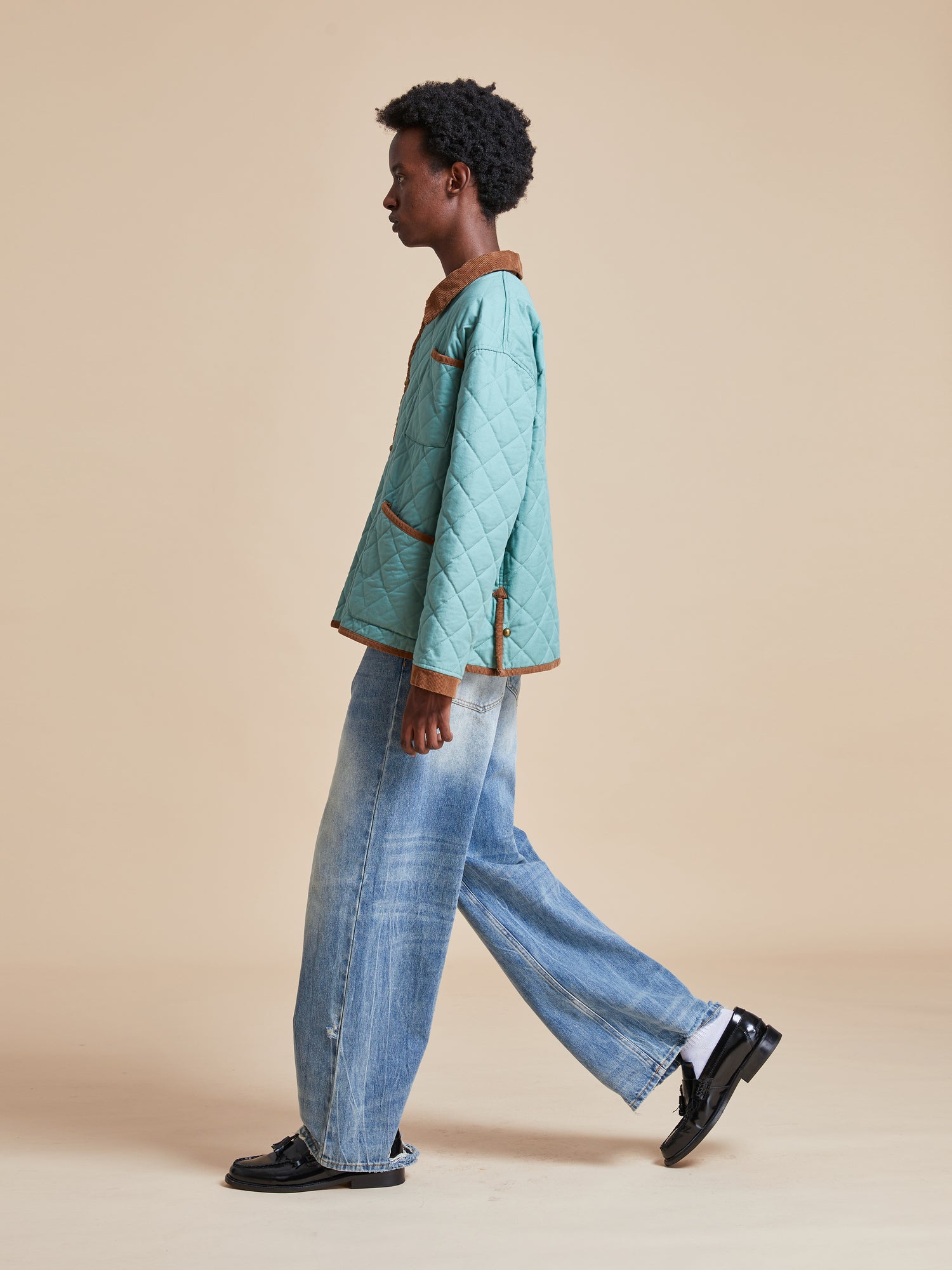 A woman in blue jeans and a Kashmir Meadow Quilt Jacket by Found walking on a beige background.