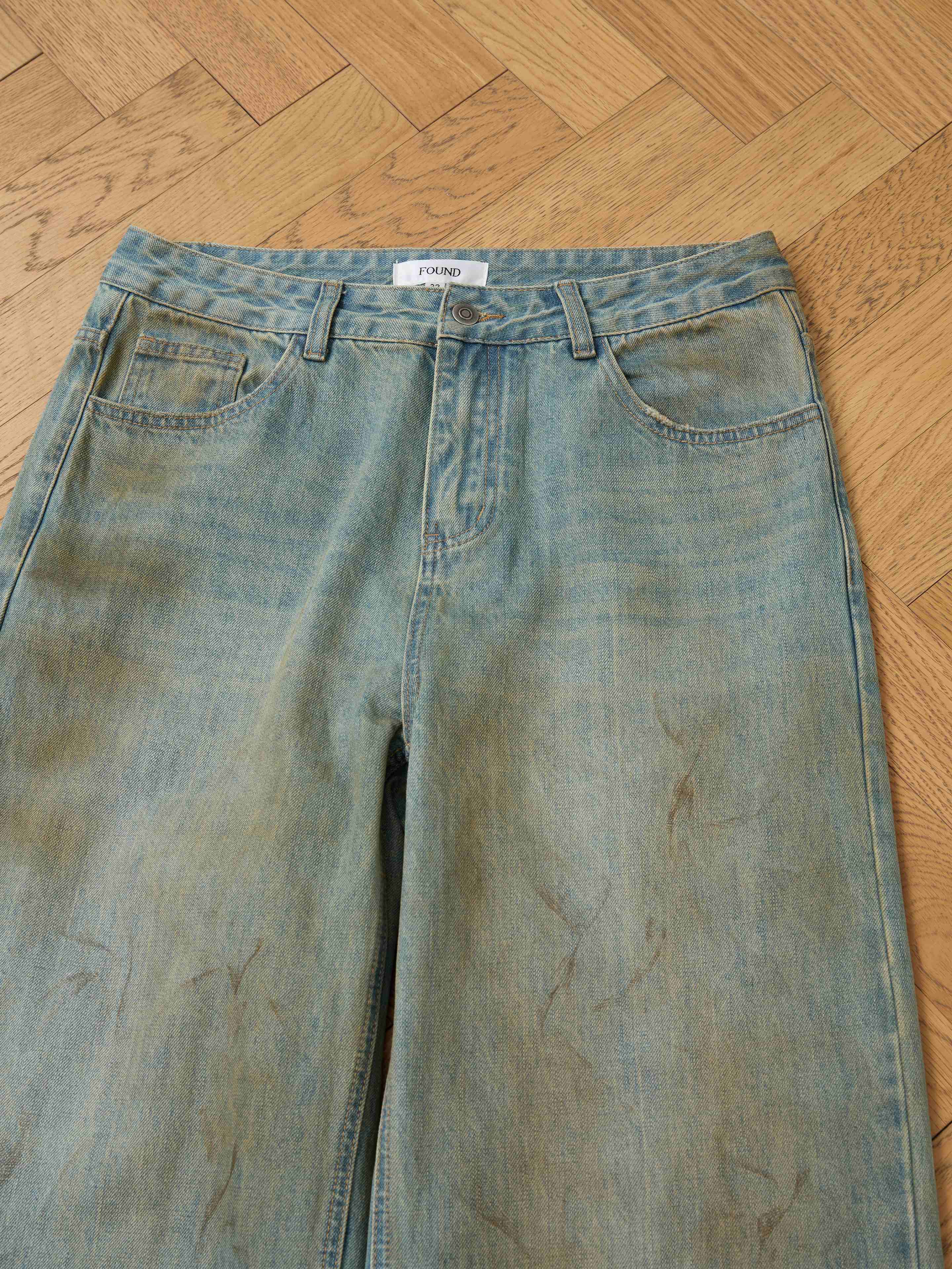FOUND’s Lacy Baggy Jeans in light blue, featuring a relaxed fit with subtle fading and creases, are displayed flat on a wooden herringbone floor.