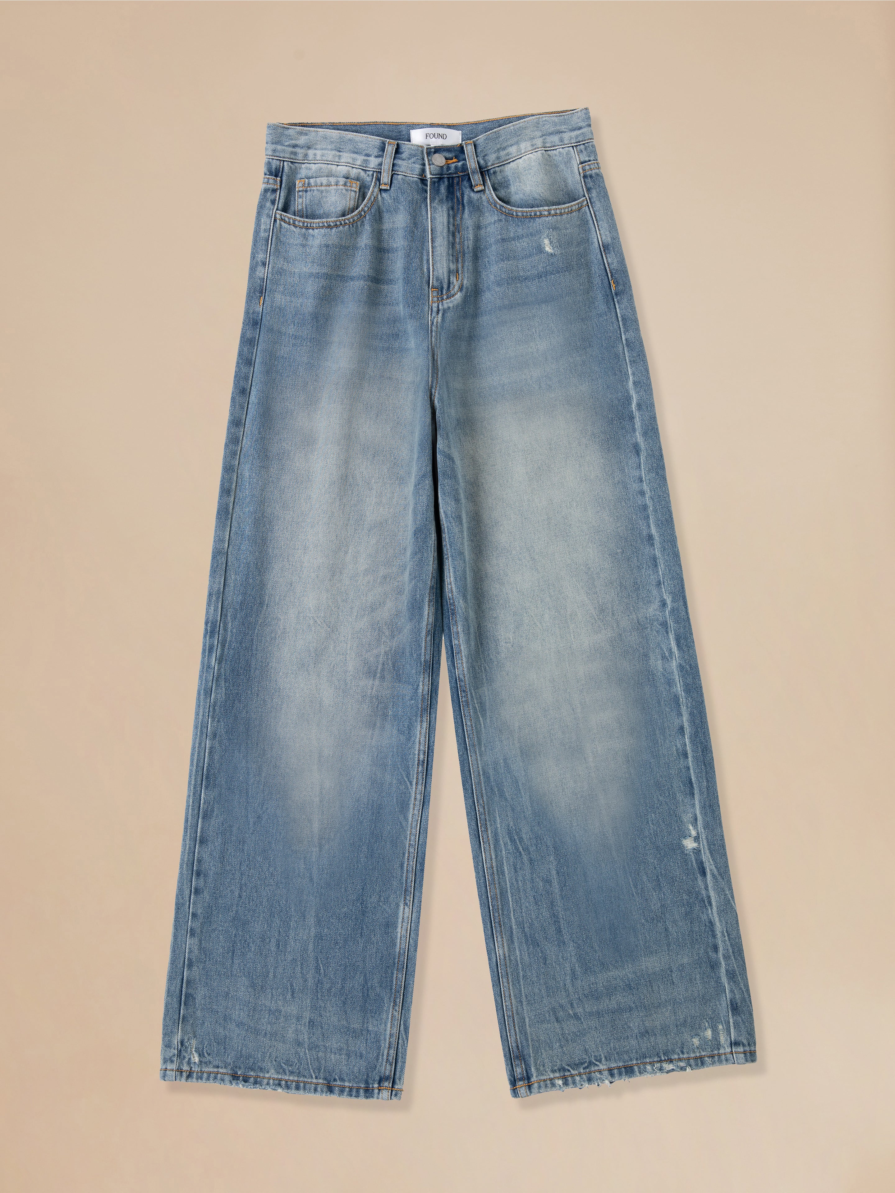 A pair of Found Lacy Baggy Jeans with distressed hems on a beige background.