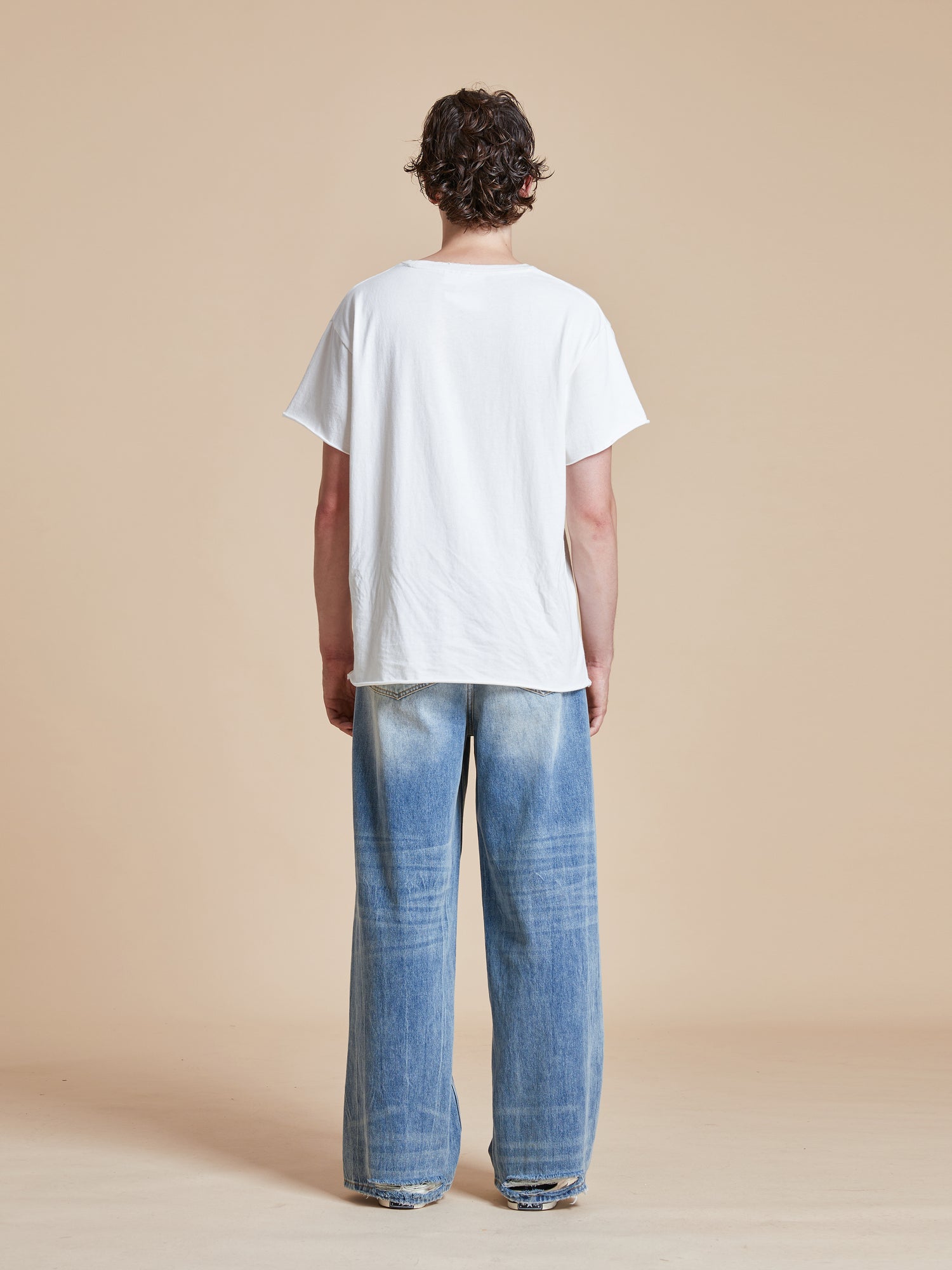 The back of a man wearing Found's Lacy Baggy Jeans with distressed hems and a white t-shirt.