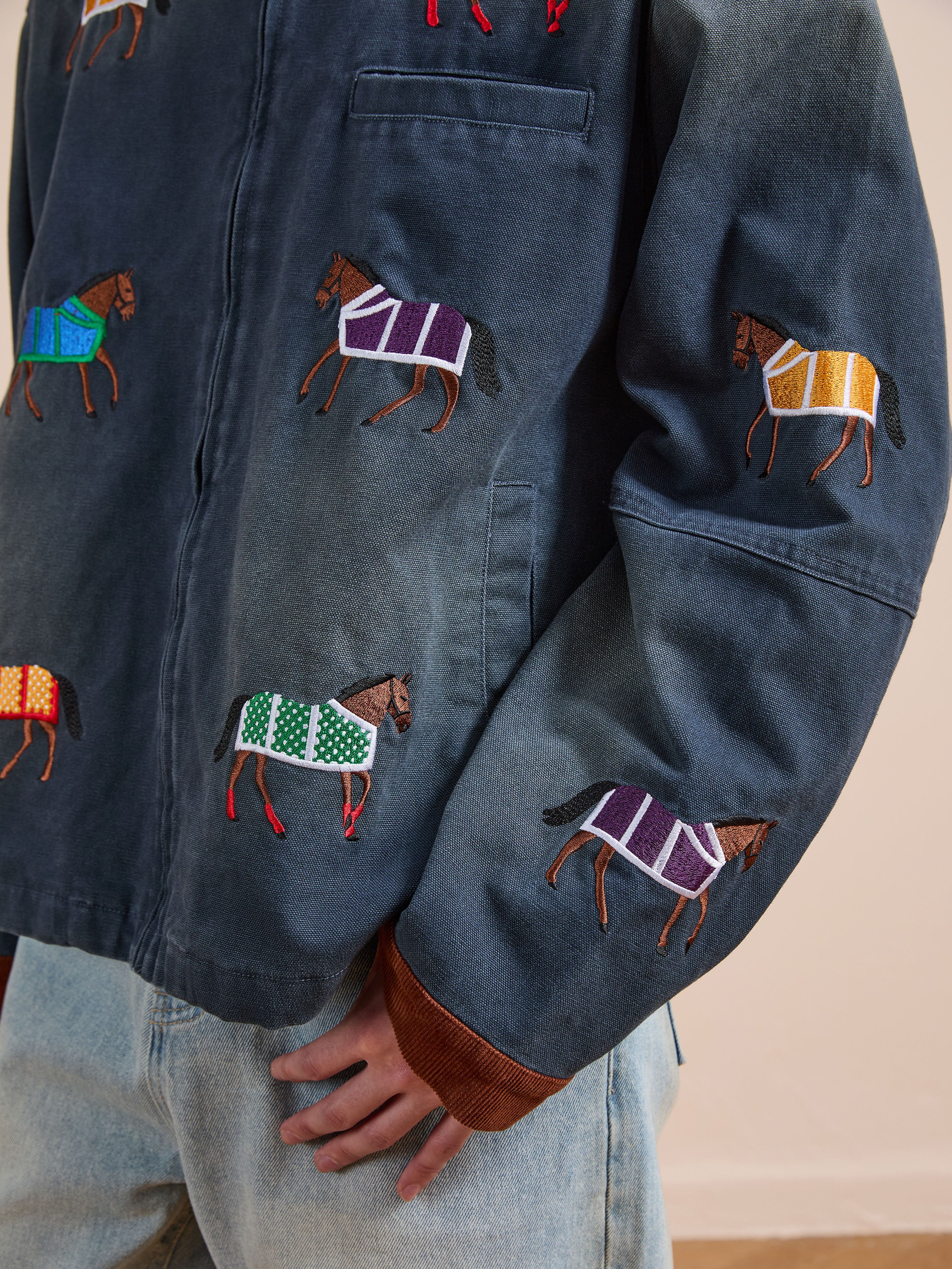 A person wearing Found's Lariat Horse Embroidered Work Jacket in unisex navy, featuring vibrant horse embroidery, paired with light blue jeans.