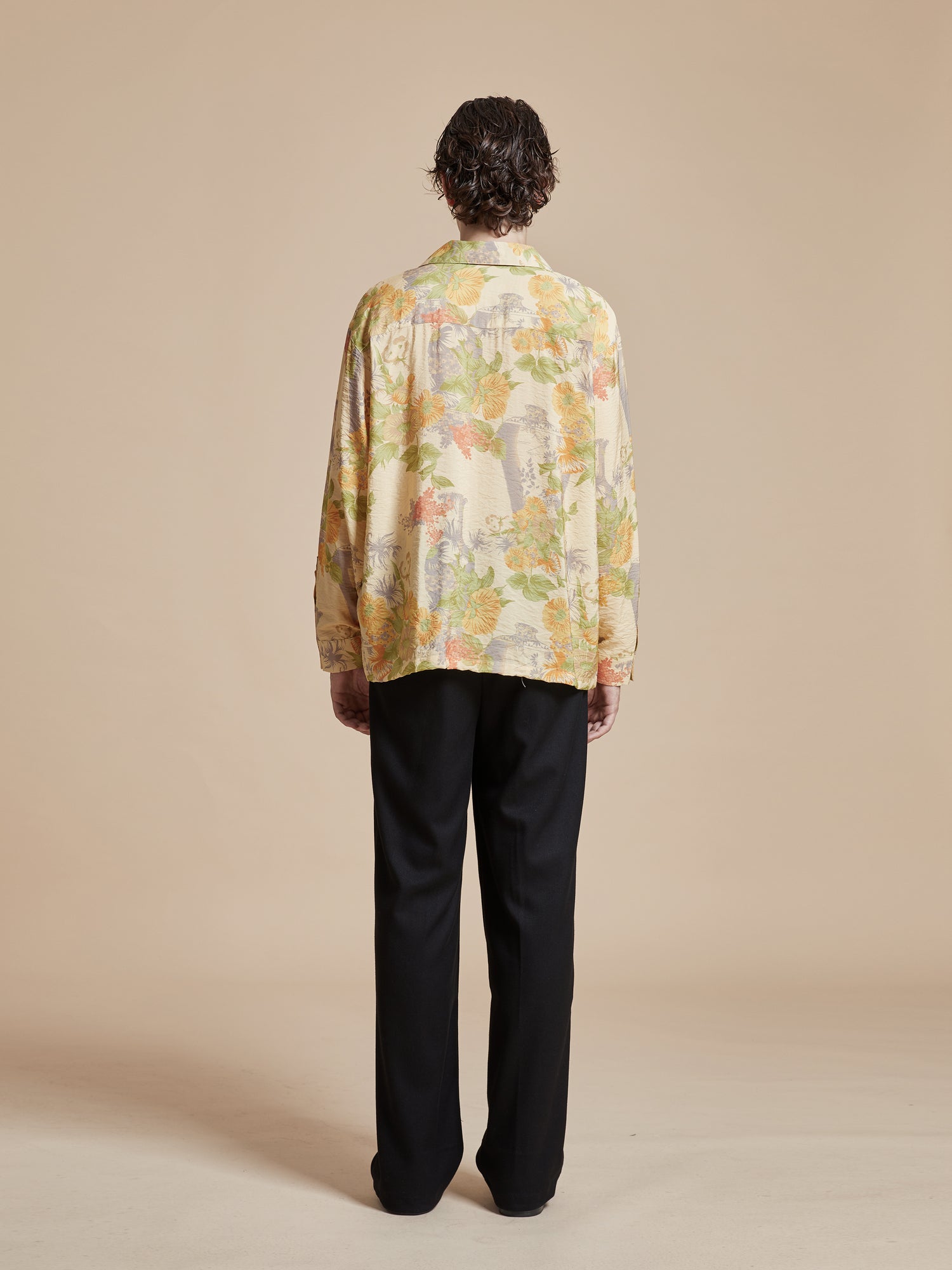 The back view of a man in a yellow floral Found Meraj Vase Pot Long Sleeve Camp Shirt adorned with Phulkari motifs.