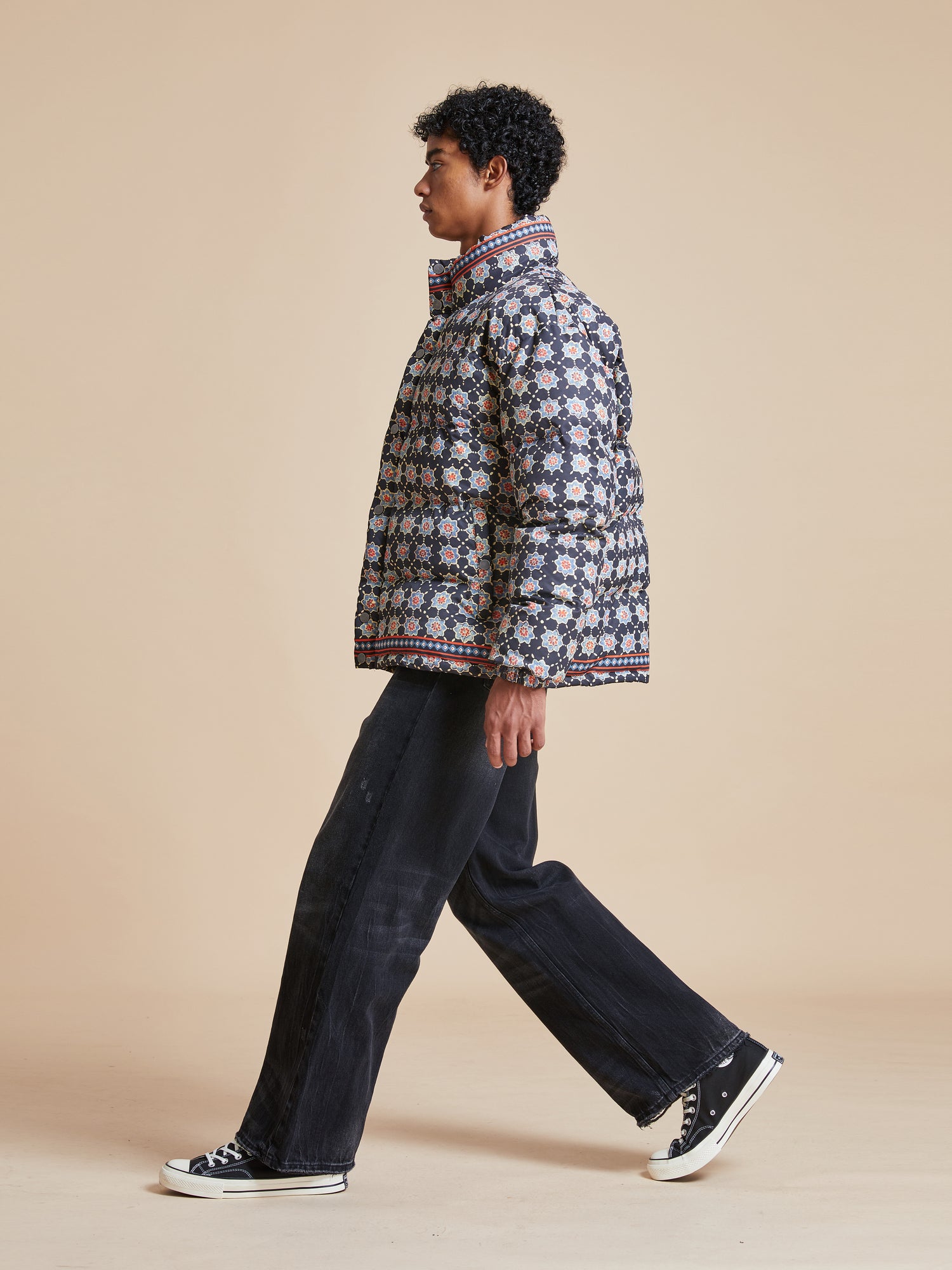 A man in a black jacket and black pants showcasing a Found Ajrak Block Puffer Jacket on a beige background.