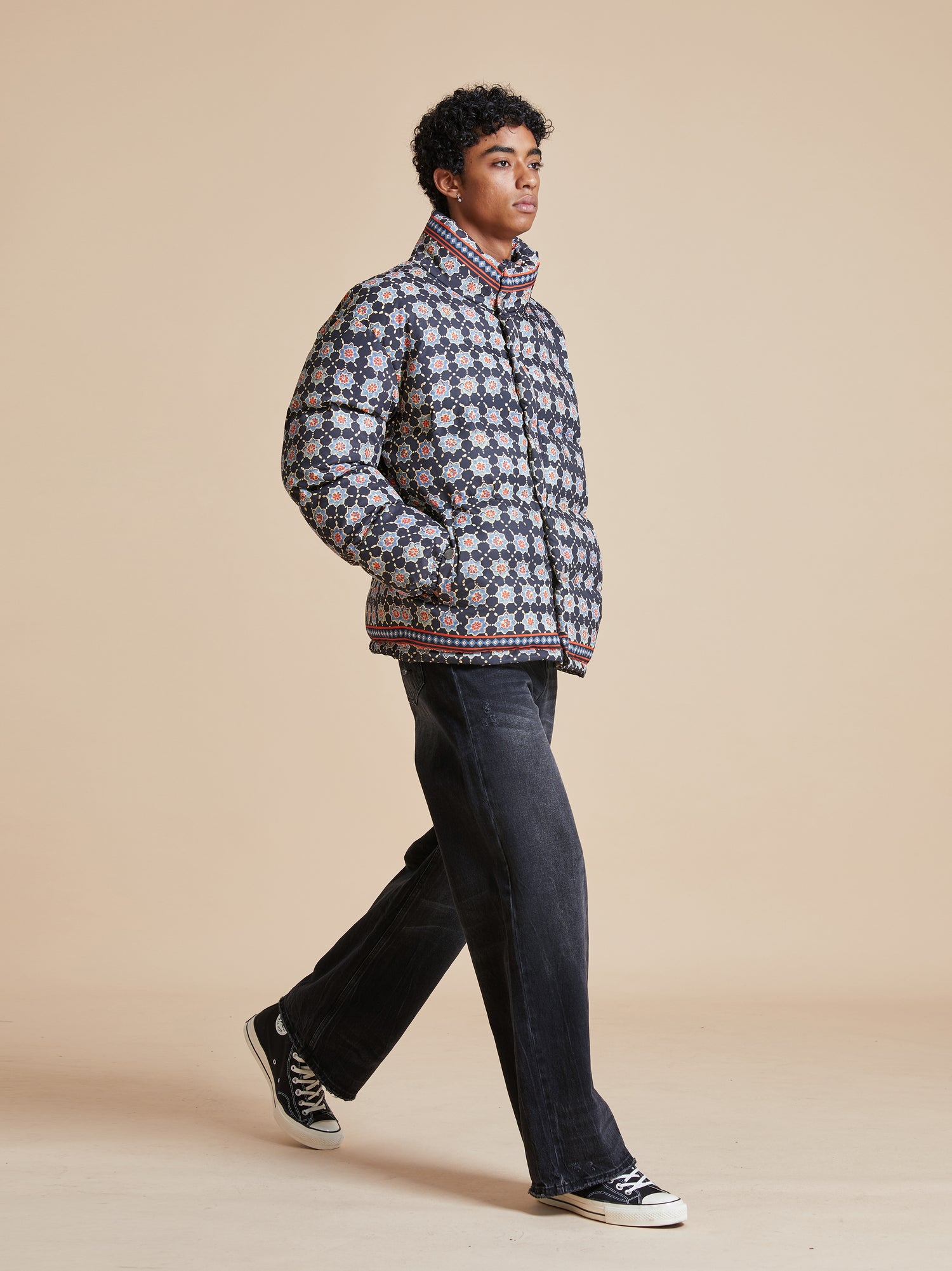 A man in a blue and white patterned Found Ajrak Block Puffer Jacket walking on a beige background.
