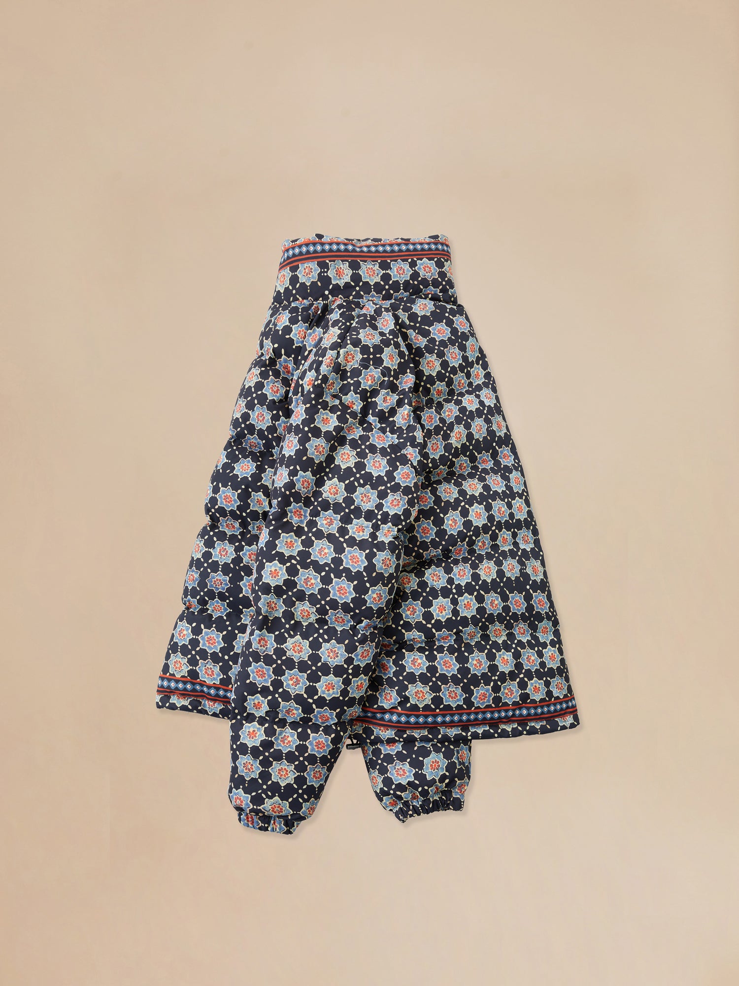 An Ajrak Block Puffer Jacket by Found, in a blue and white patterned skirt on a beige background with Pakistani block-printed patterns.