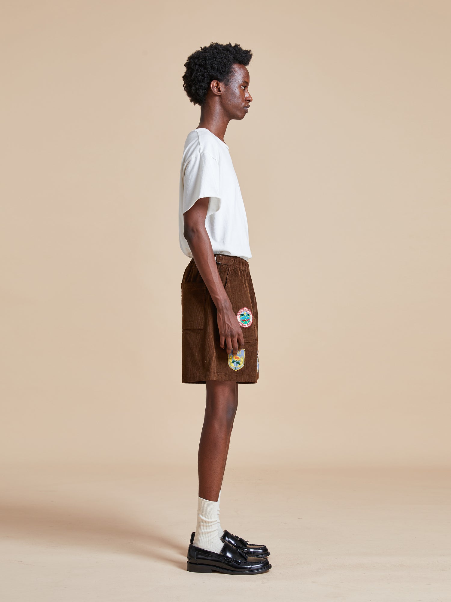 The model is wearing a white t - shirt and Found's Canoe Multi Patch Corduroy Shorts.
