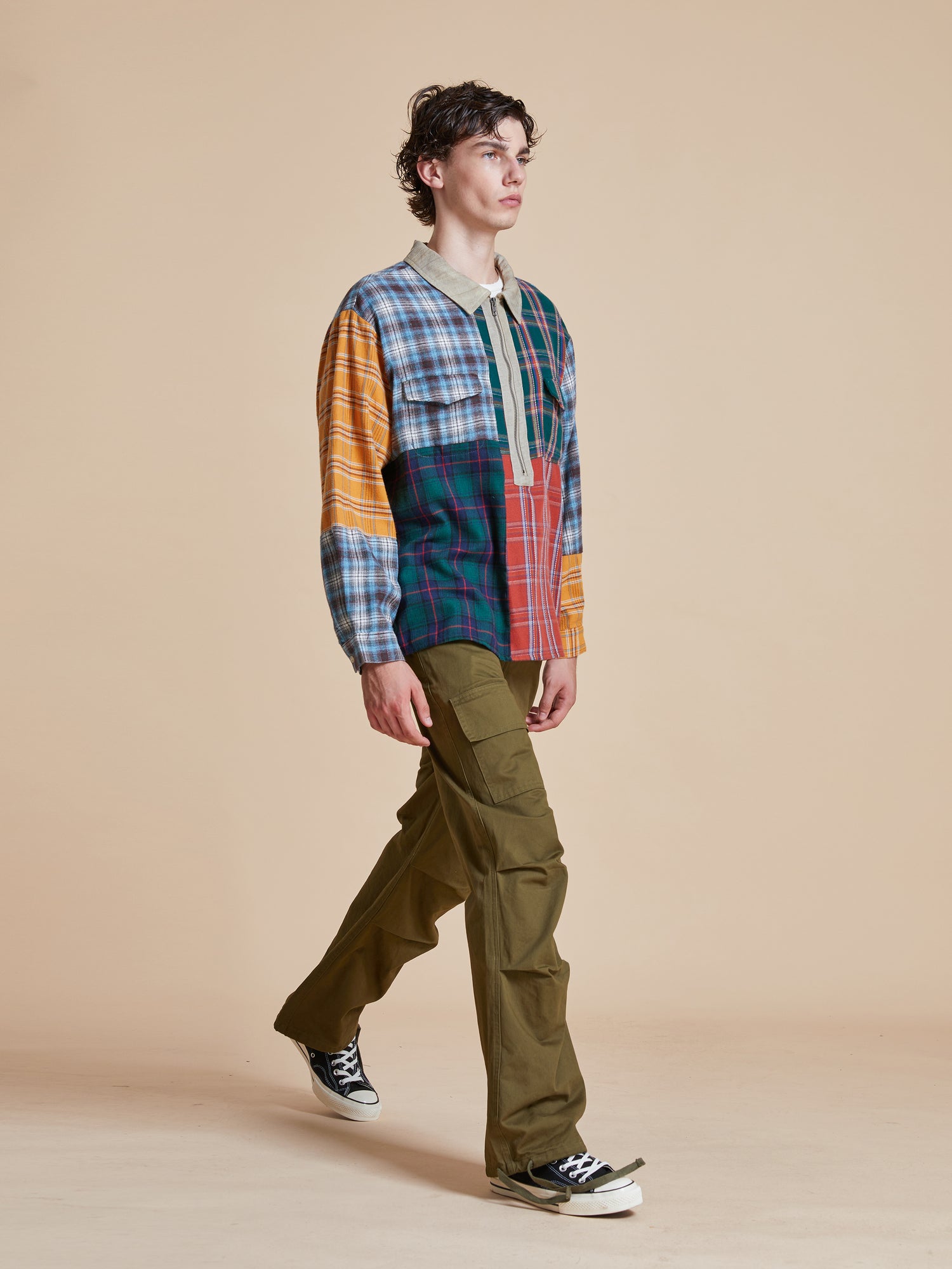 A man wearing a Found Multi Plaid Tartan Shirt and pants walking on a beige background.