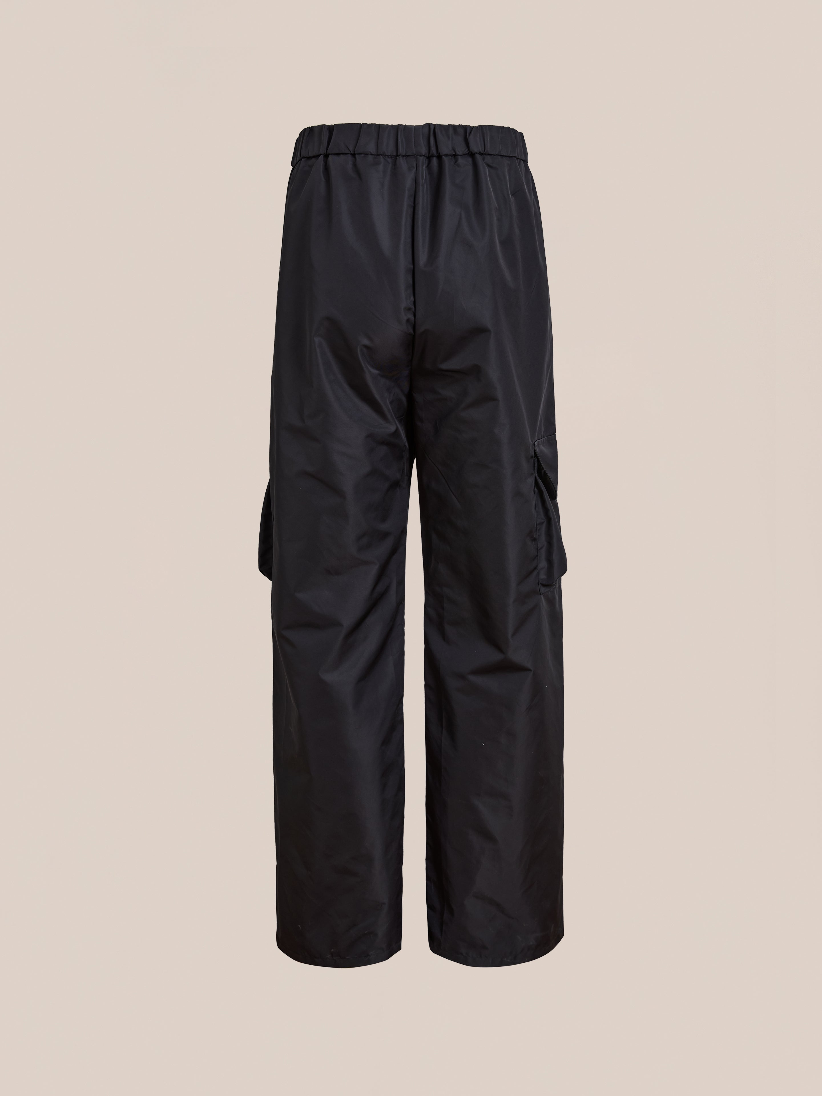 FOUND Nylon Cargo Pants in black, crafted from nylon with a relaxed fit, elastic waistband, and side pockets. Unisex design combines comfort and versatility. Shown against a plain beige background.