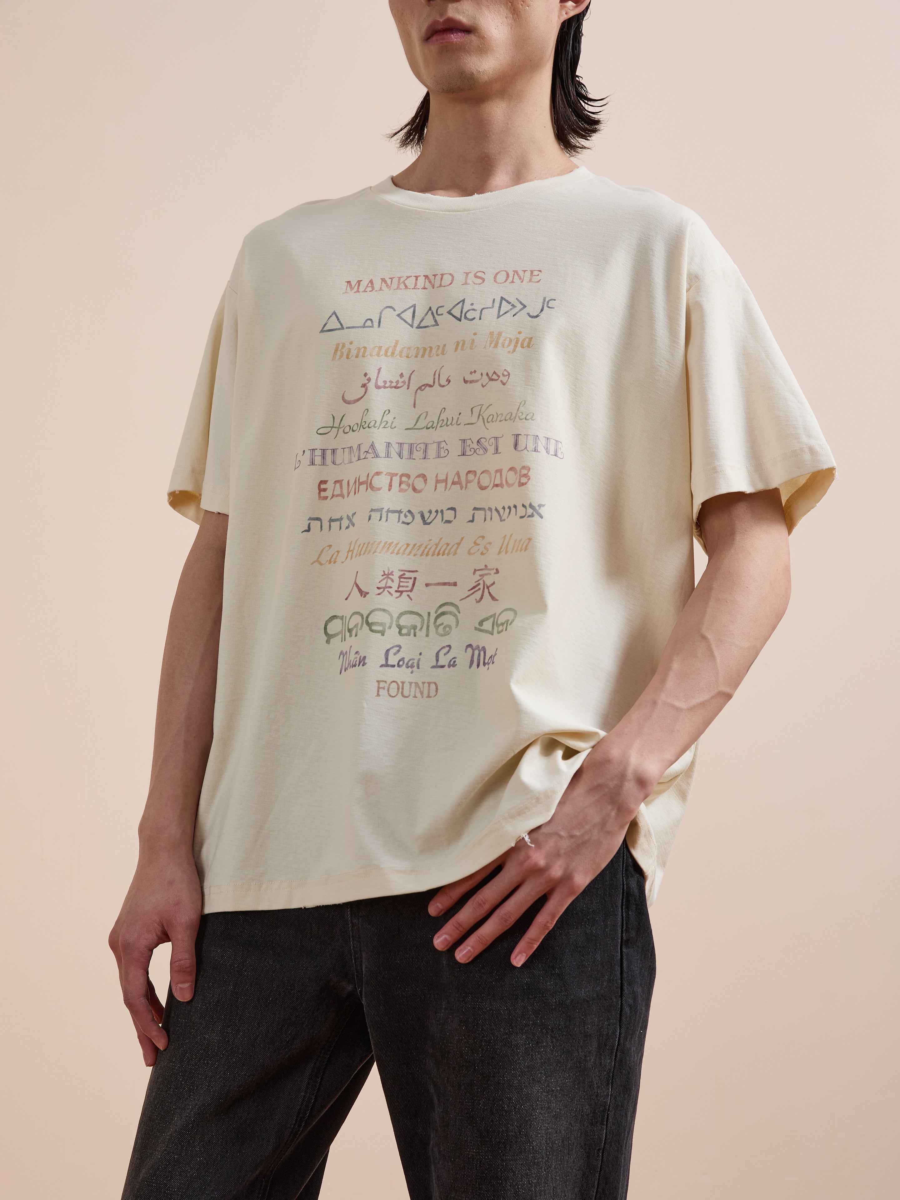 A person wears the FOUND One Humanity Tee, a unisex relaxed fit cotton t-shirt with "MANKIND IS ONE" and its translations on the front, promoting unity across cultures.