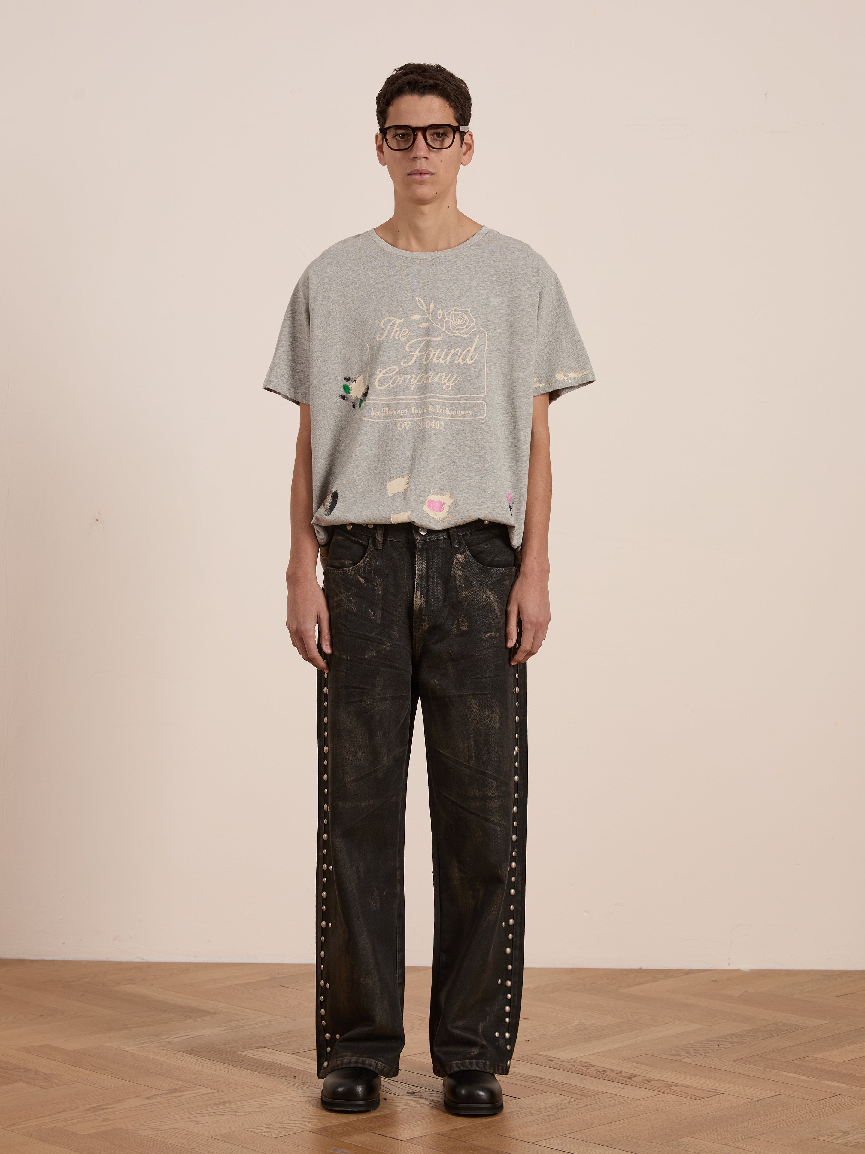 A person wearing the vintage-inspired Painters Company Tee by FOUND and slightly distressed black jeans stands against a plain background, effortlessly blending timeless style and comfort.