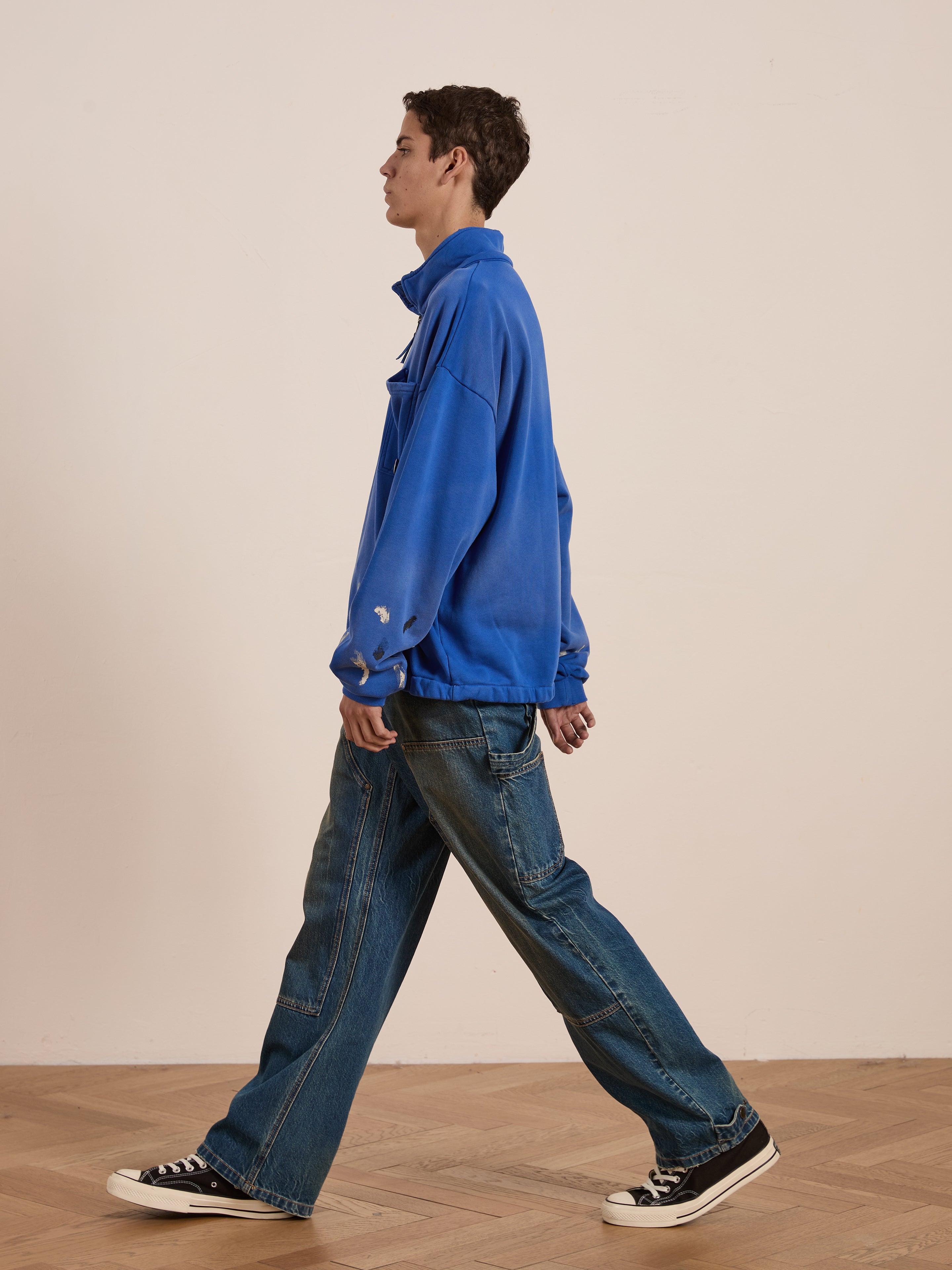 A person in a blue jacket and FOUND Denim Carpenter Jeans with utility pockets walks on the wooden floor, facing left.