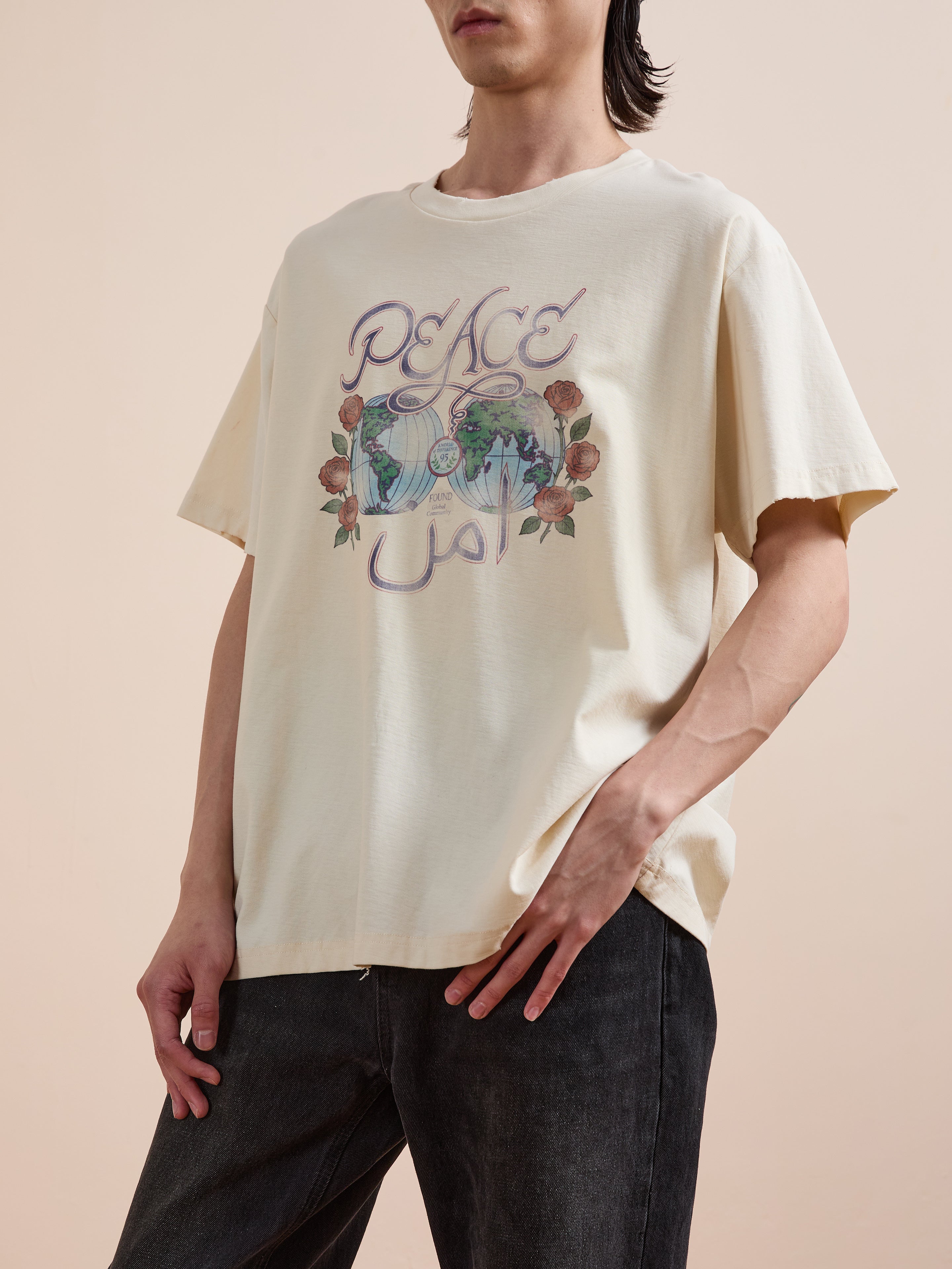 A person wears the FOUND Peace Globe Tee, a vintage cotton unisex shirt with floral graphics and "Peace" in English and Arabic, styled with black jeans for a relaxed, comfortable look.