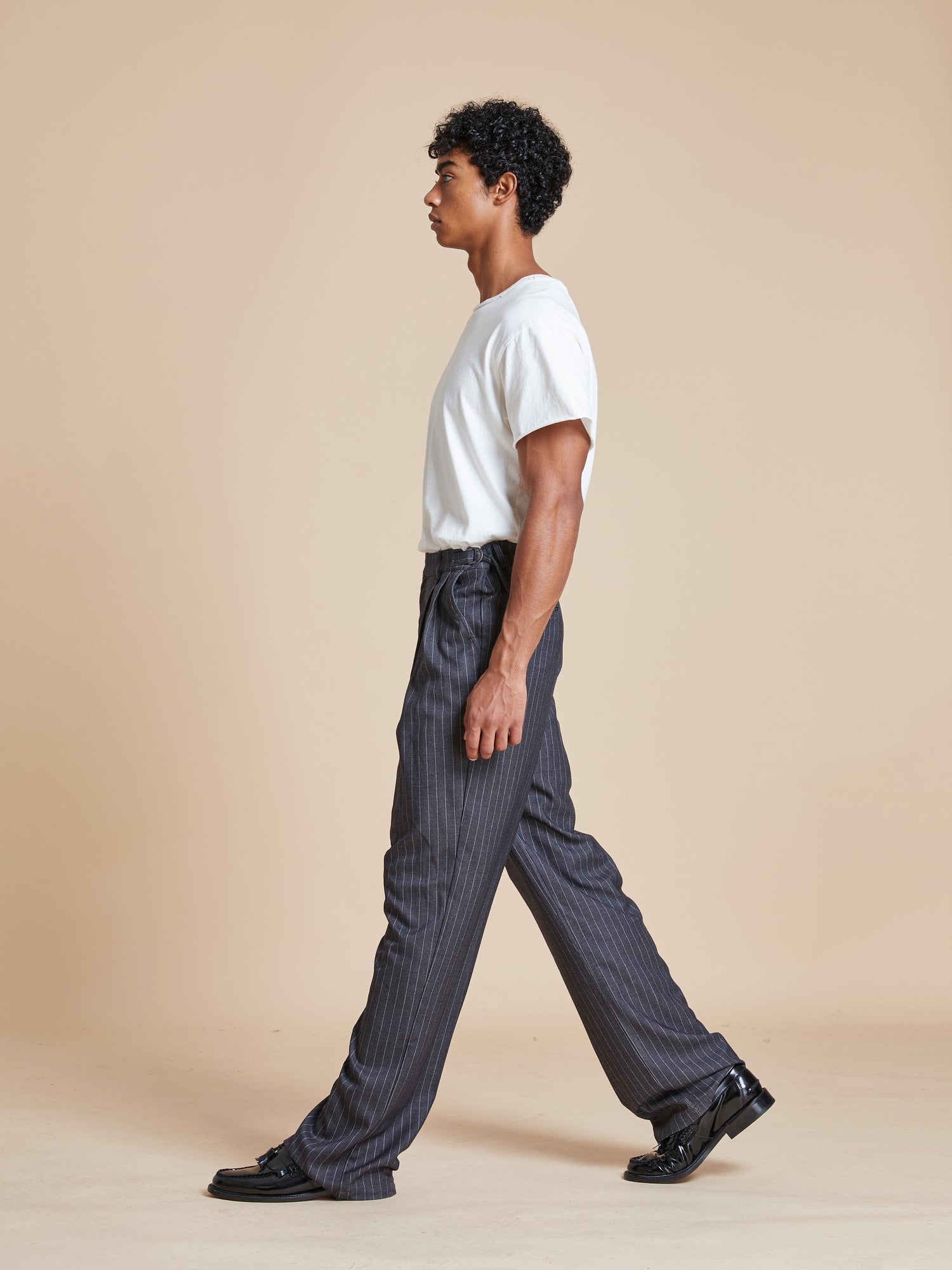 A man wearing a white t-shirt and Found Pinstripe Pleated Trousers.