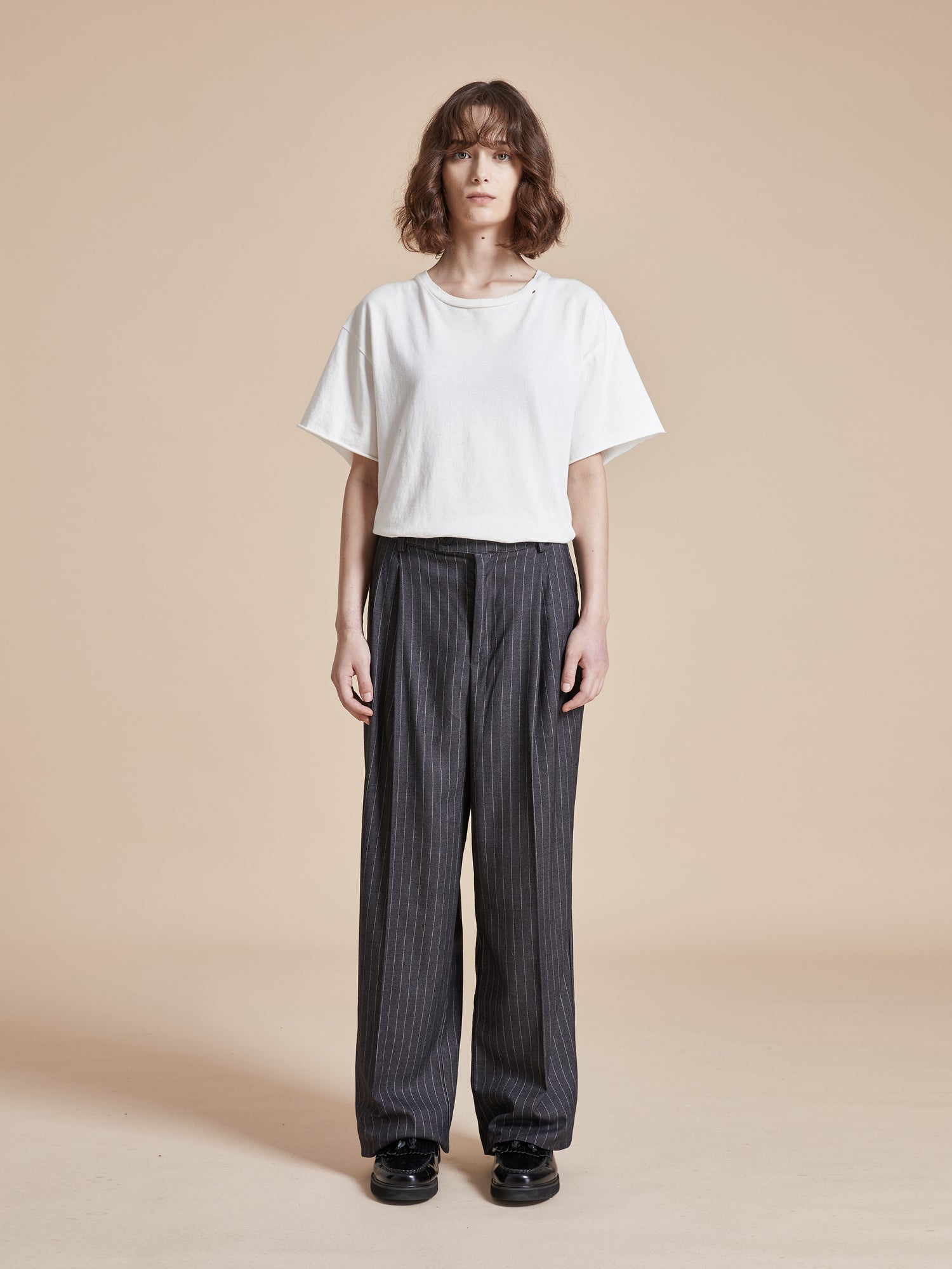 A model wearing a white t-shirt and Found Pinstripe Pleated Trousers.
