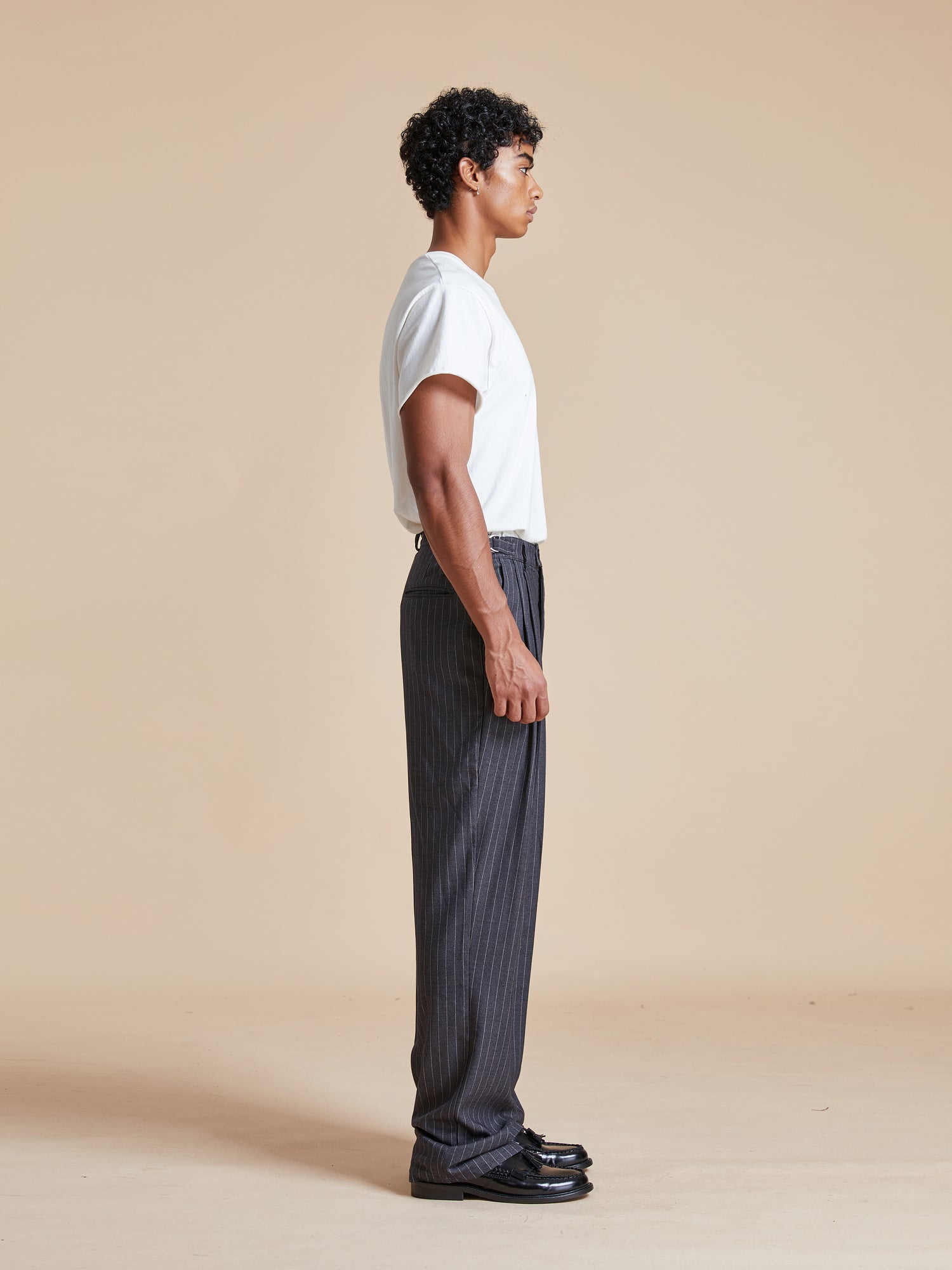 A man wearing a white t-shirt and black Found Pinstripe Pleated Trousers.