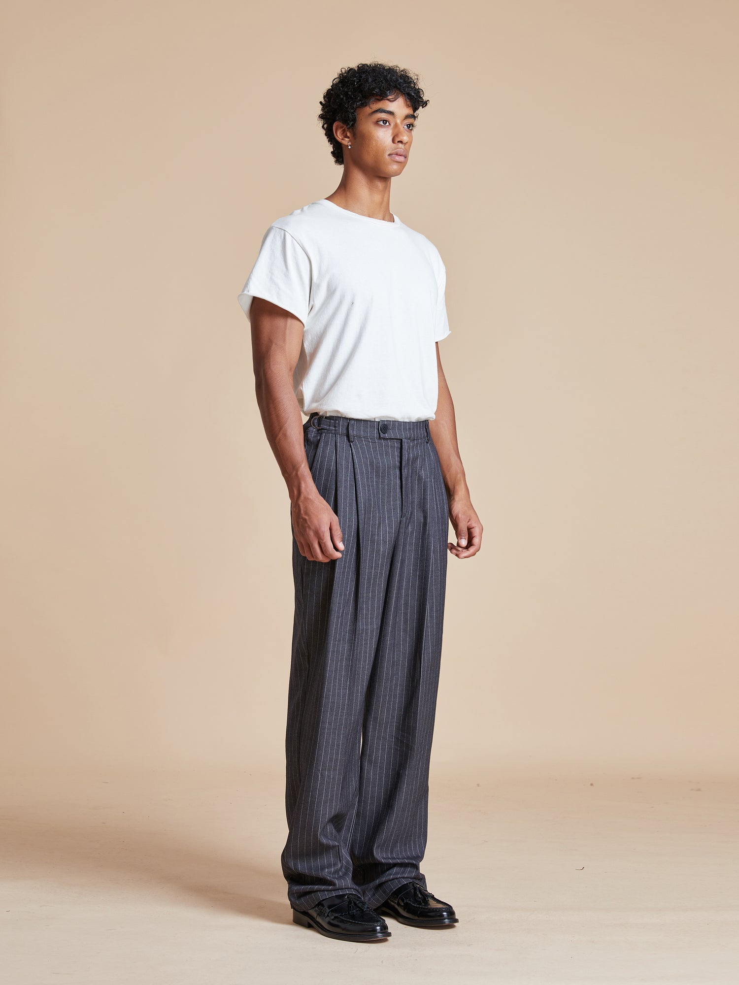 The model is wearing a white t - shirt and grey Found Pinstripe Pleated Trousers.