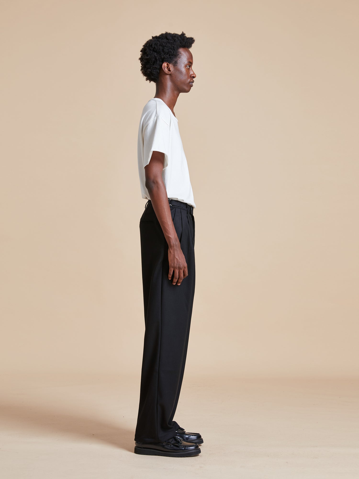 A man wearing black Pleated Trousers and a white t - shirt from Found.