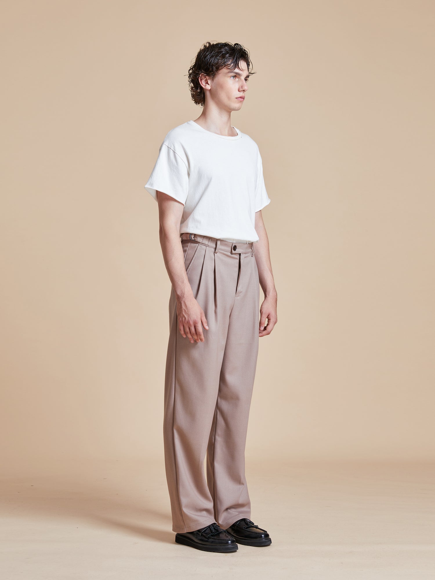 The model is wearing a white t - shirt and beige Found Pleated Trousers.