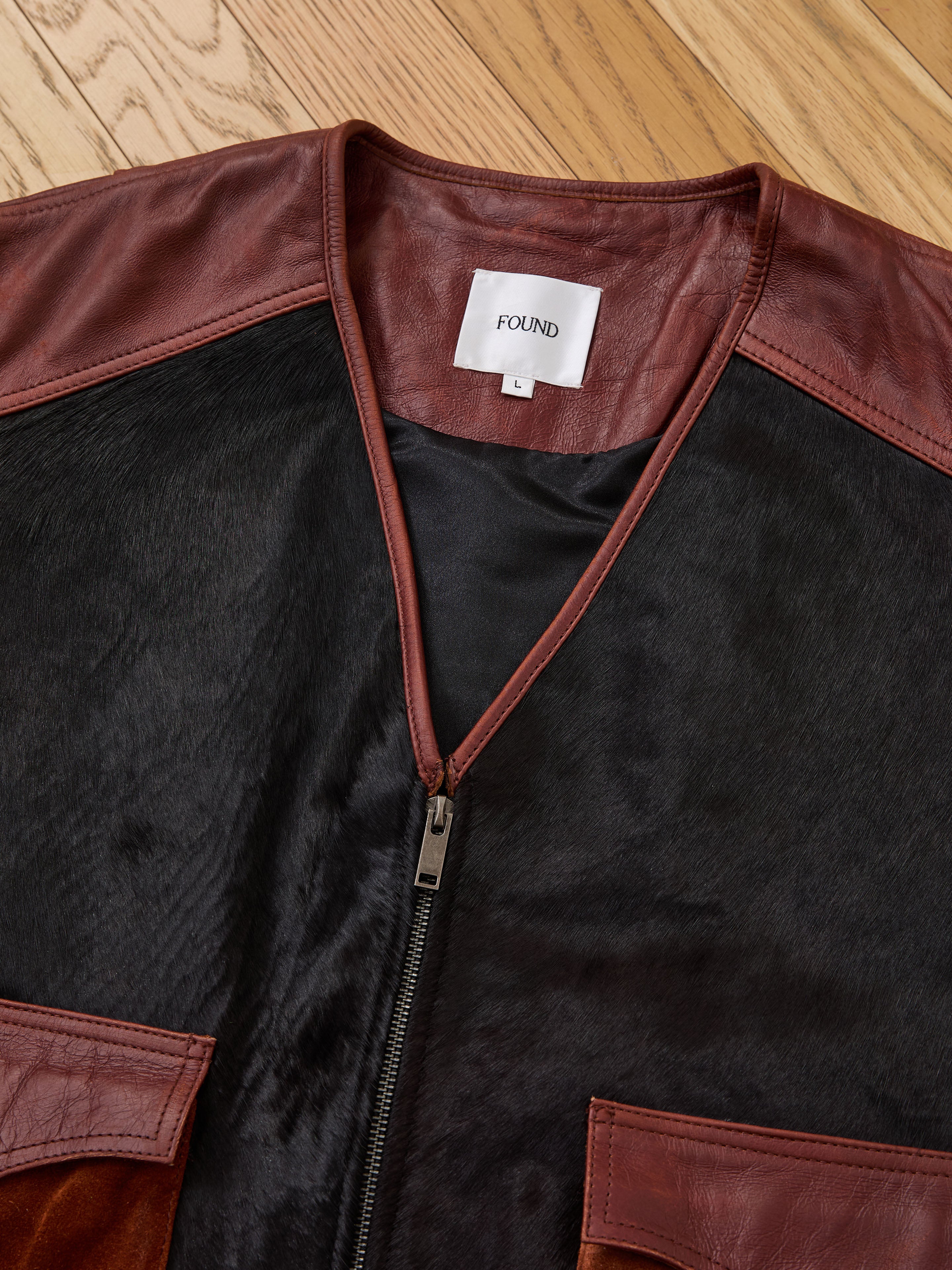 A close-up of a brown and black Found Fur Western Leather Vest, size L, displayed on a wooden floor.
