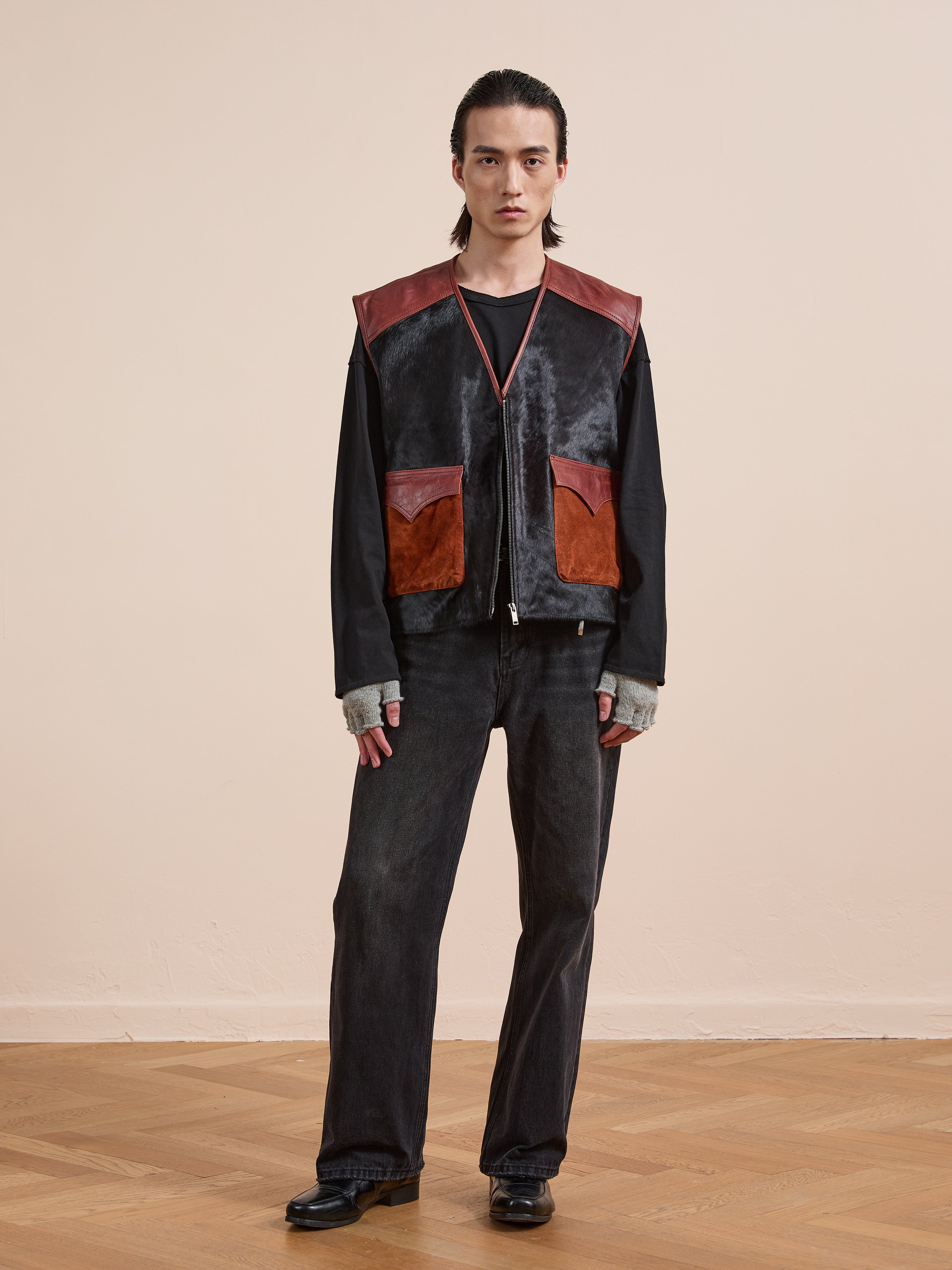 A person stands indoors wearing black jeans, a black long-sleeve shirt, and the Found Fur Western Leather Vest featuring two large front pockets and leather details.