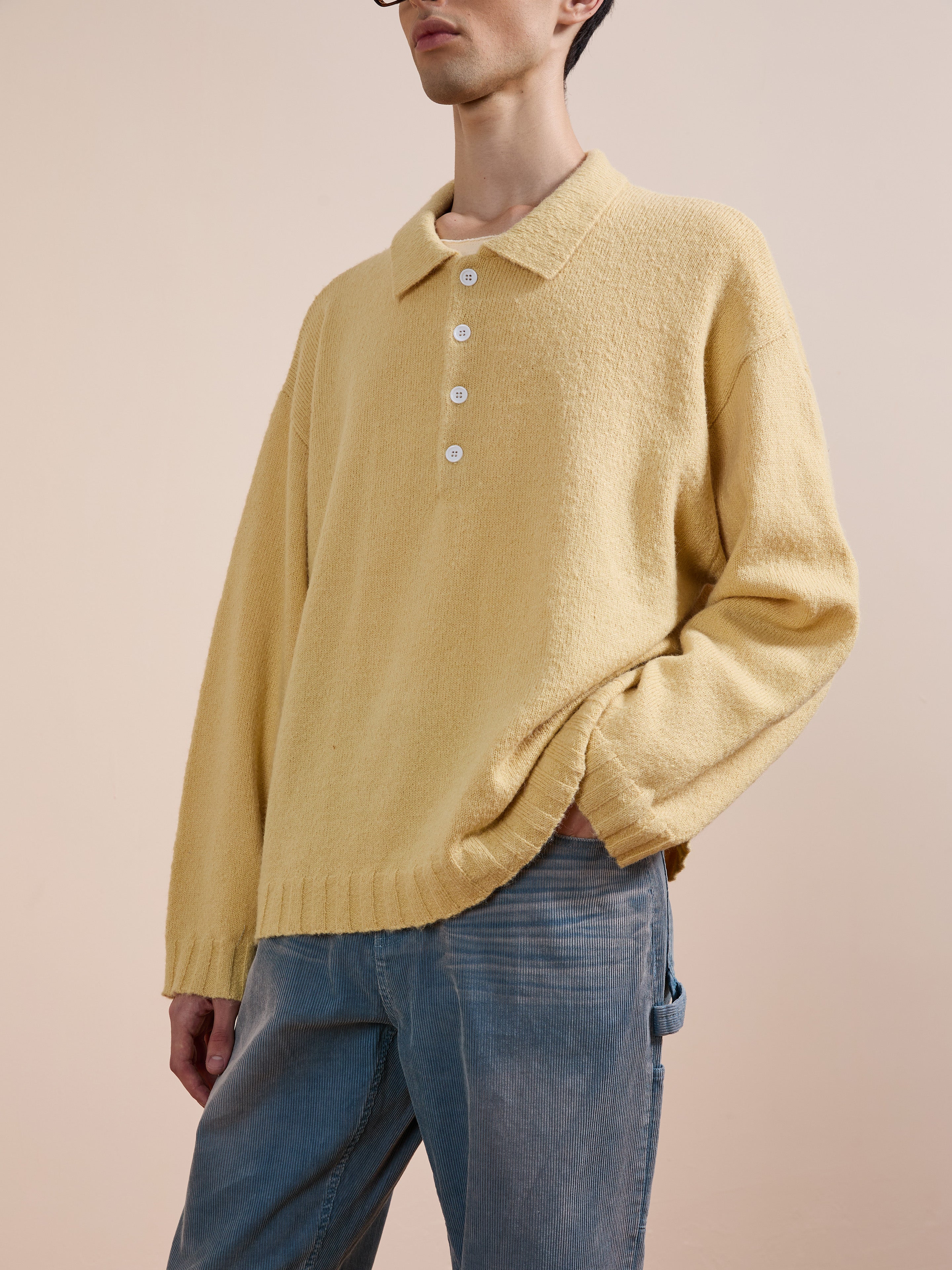 A person wears the FOUND Knit LS Polo Sweater in yellow with white buttons, crafted from brushed knit fabric, paired with light blue jeans against a neutral background.
