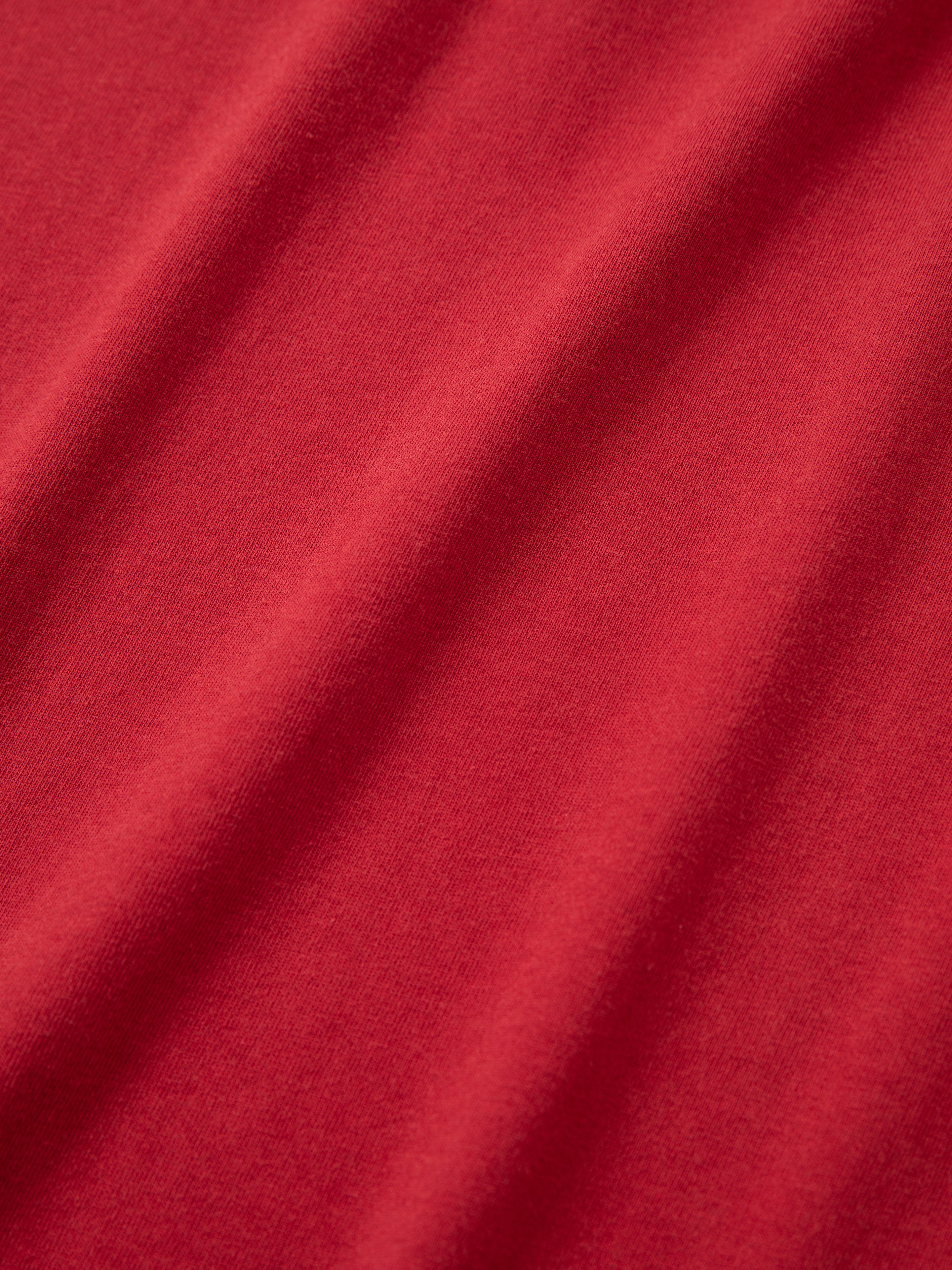 A close-up view of the Embroidered Henley from FOUND, showcasing its red fabric with visible texture and slight creases.