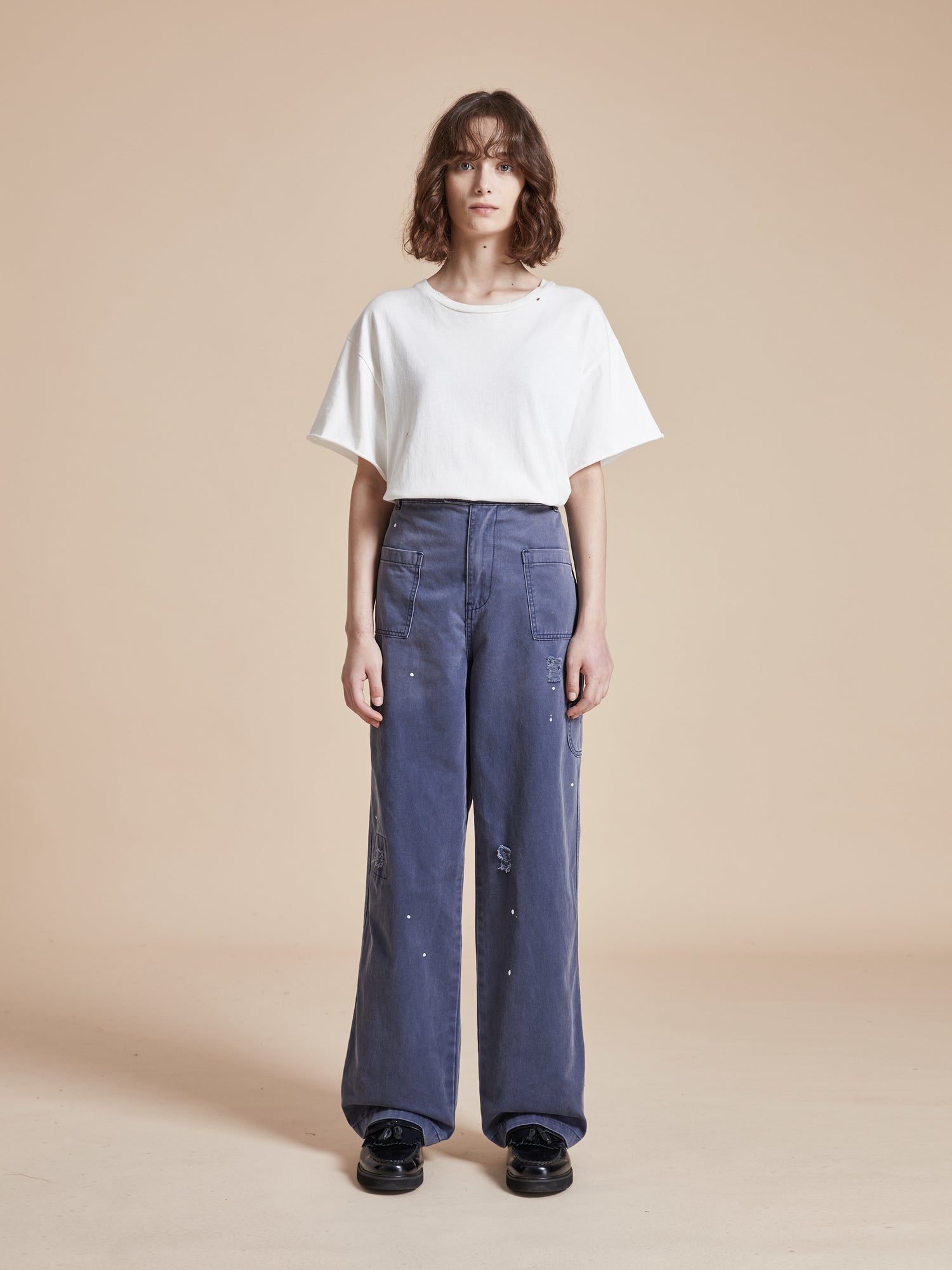The model is wearing a white t - shirt and blue Found River Painters Chore Pants.